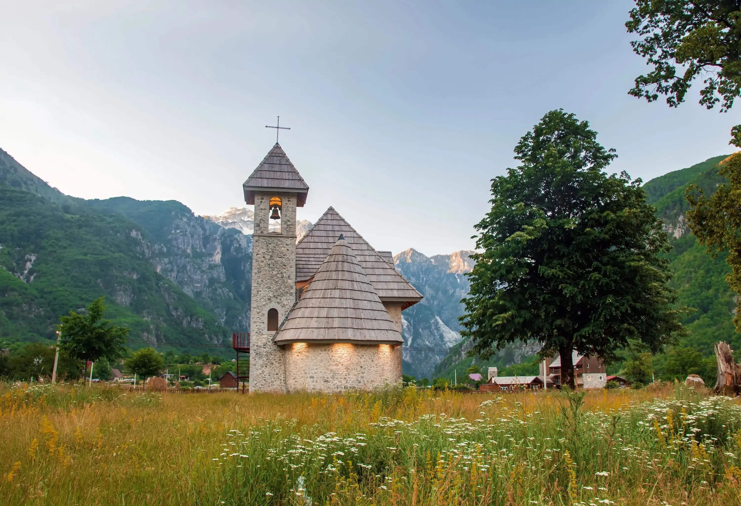 Ancient orthodox church in a field by a tree by a mountain range on a sunny day