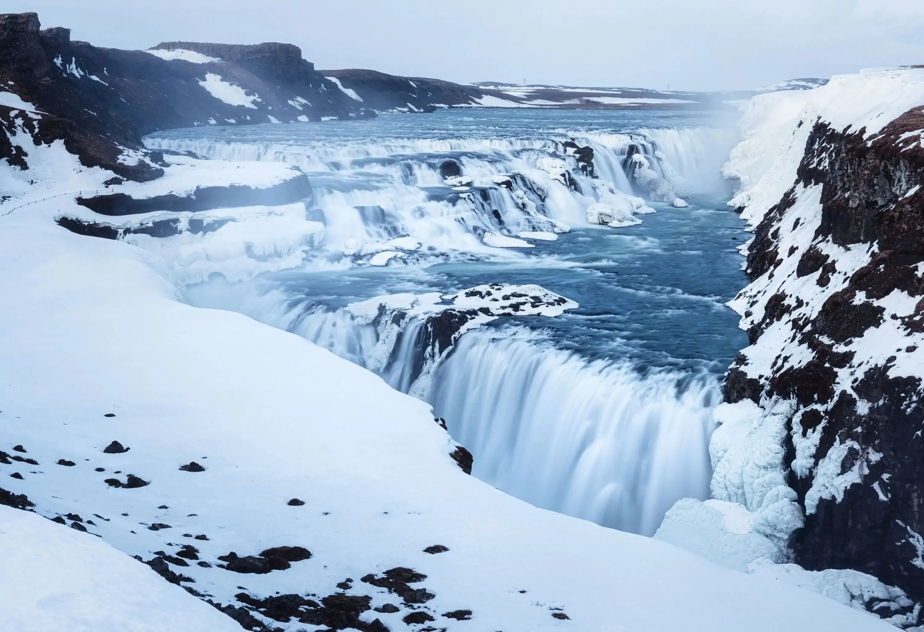 Wide and dramatic waterfall on a grey day in winter covered in ice and snow