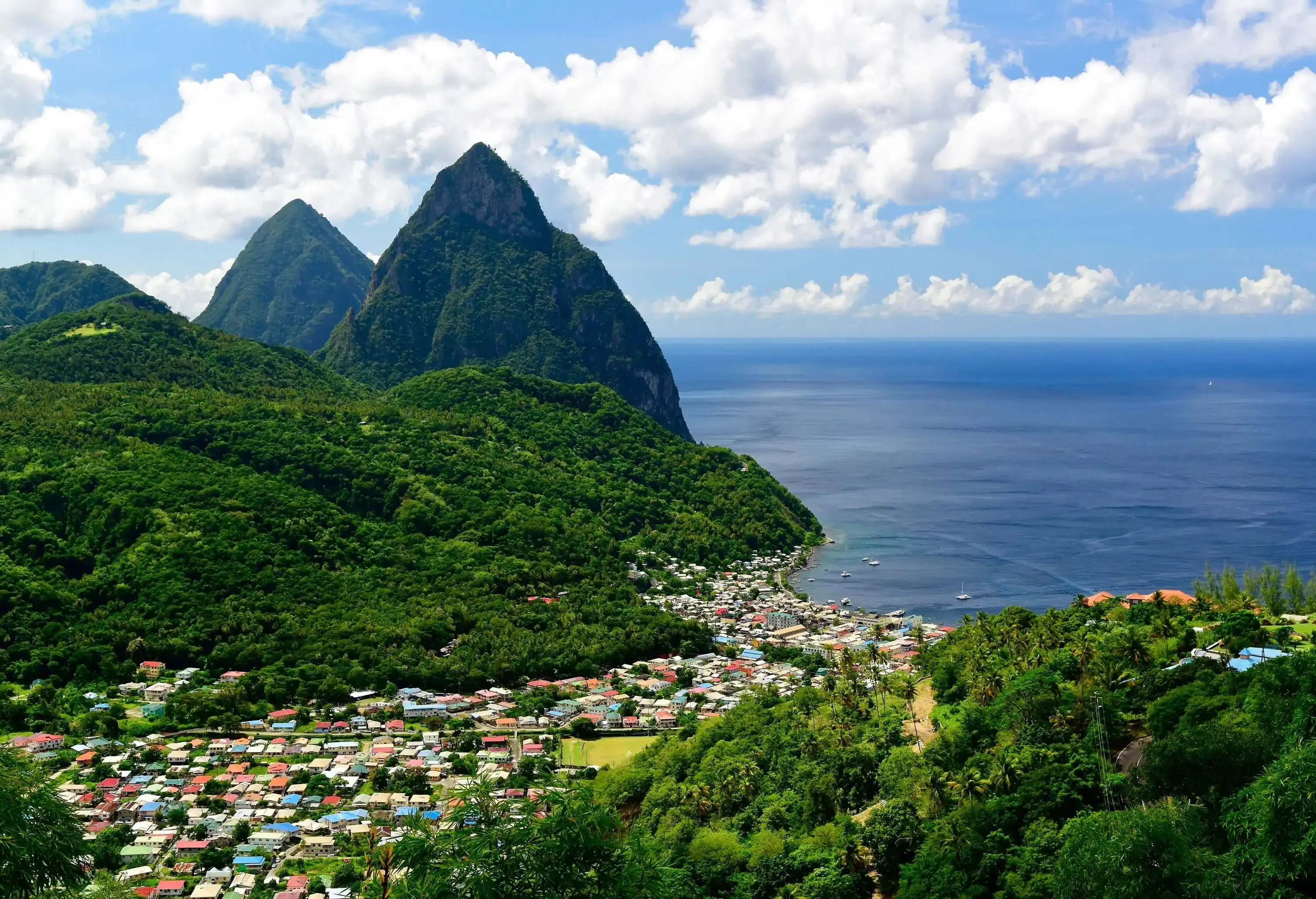A picturesque coastal town nestled in a paradise with a verdant and mountainous island surrounded by the tranquil sea under the cloudy blue sky.