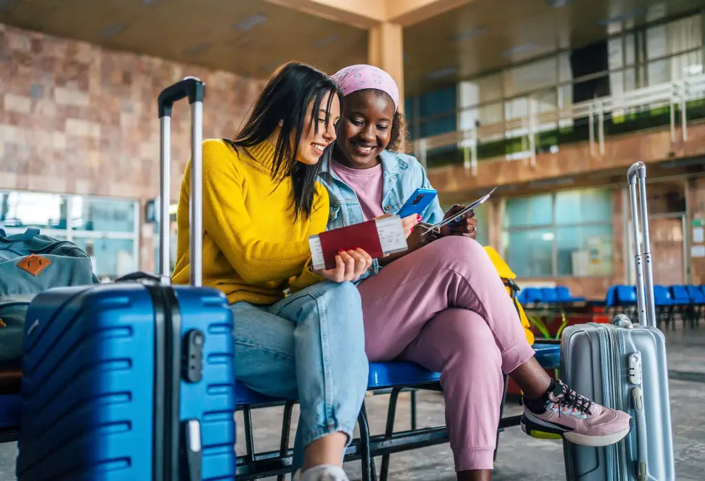 Young cheerful multi racial women friends looking at mobile phone at the airport while waiting for their flight
