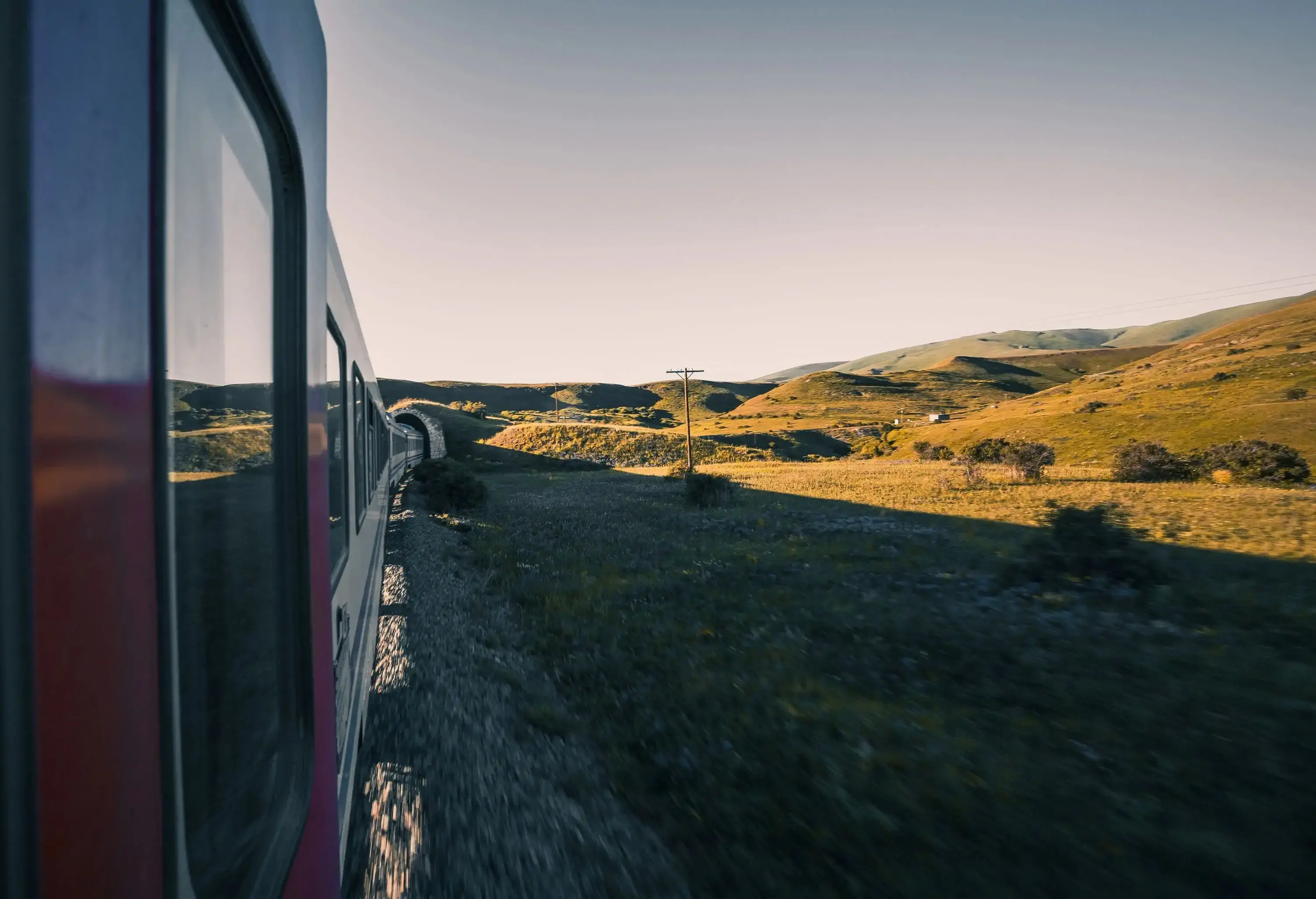 A window view of a train going inside a tunnel in a hilly area.