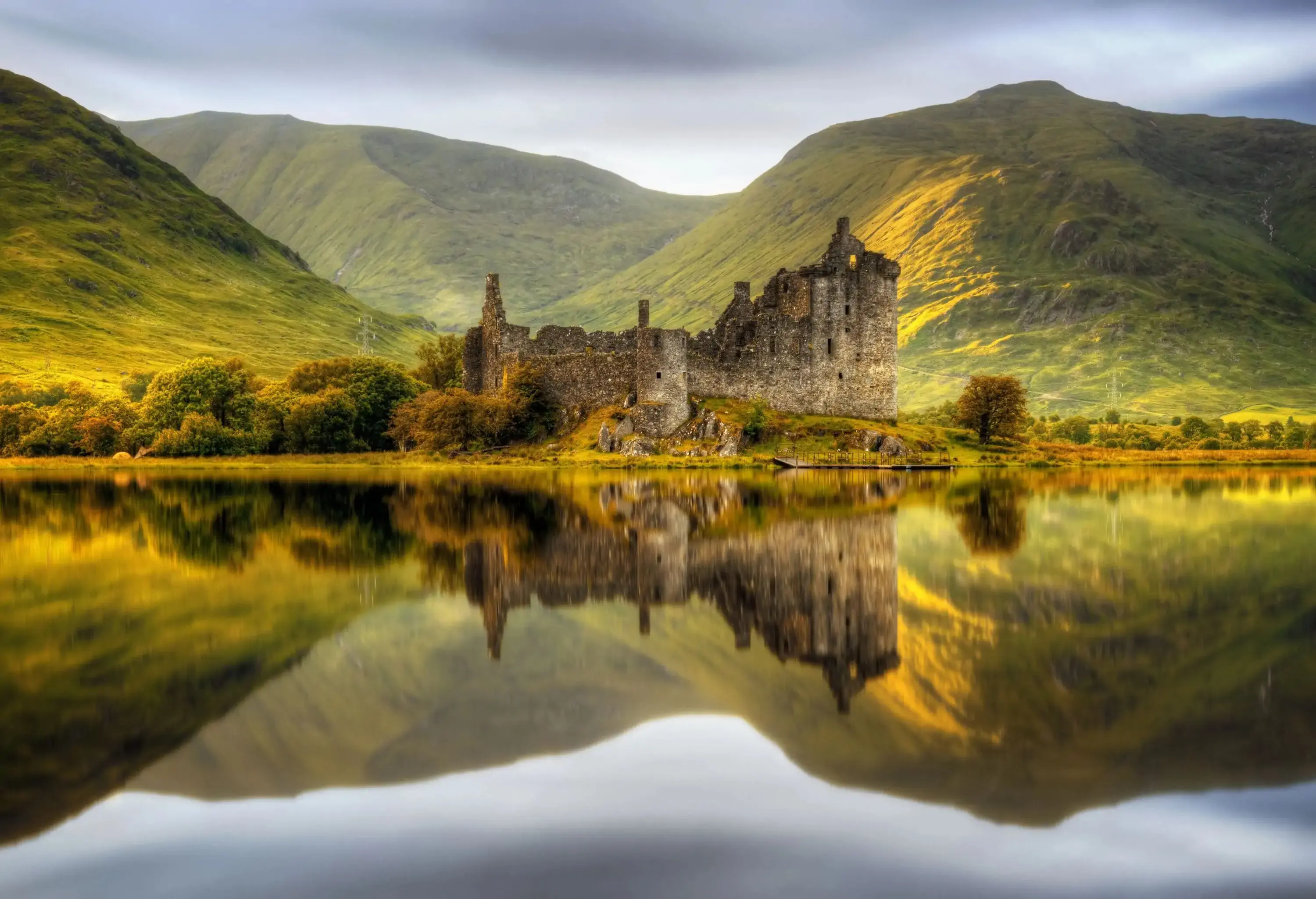 View of an ancient castle reflected in a lake with green hills in the background