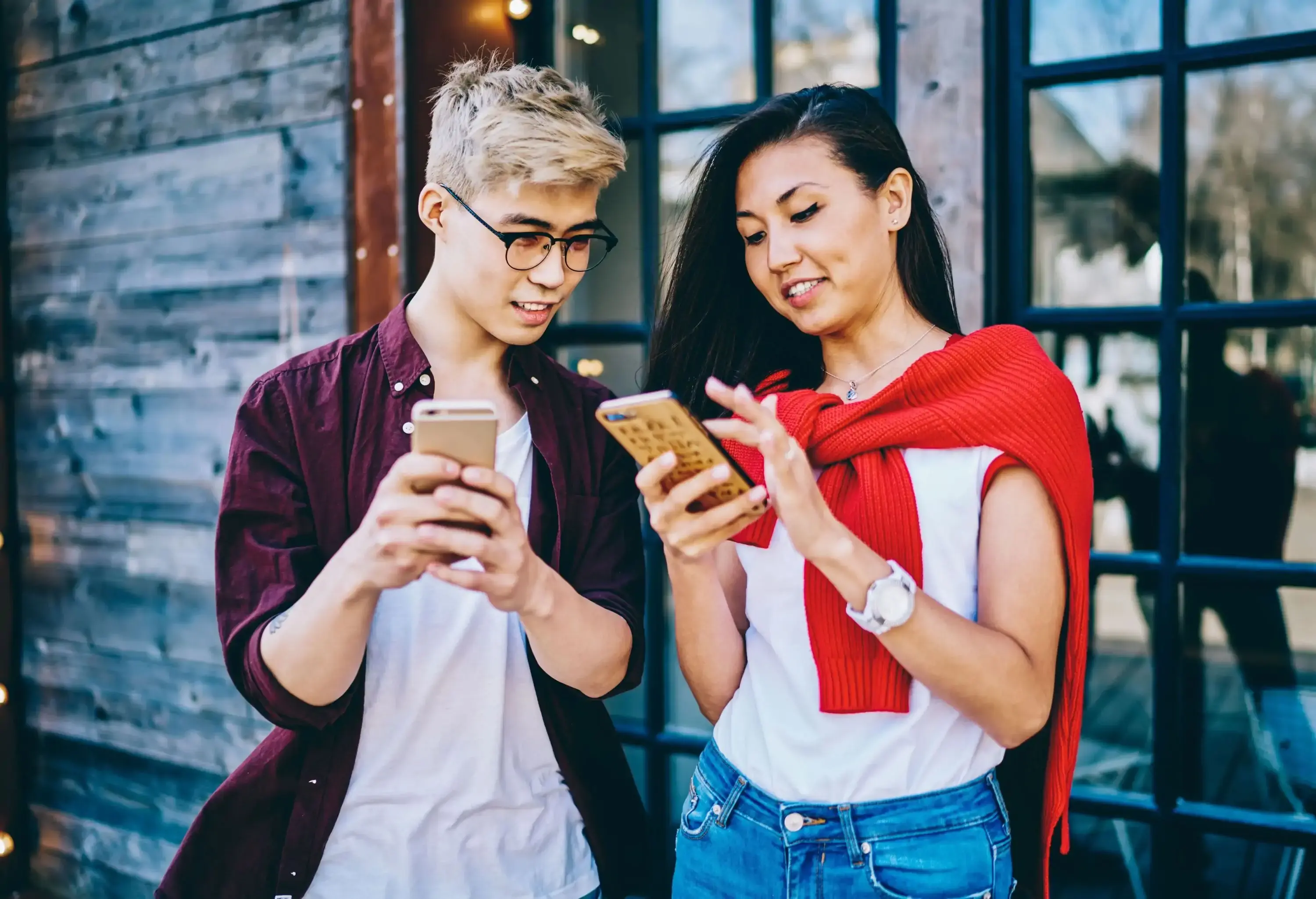 Content happy smiling Asian couple dressed in casual clothes white t shirts watching mobile phones walking in street in summer