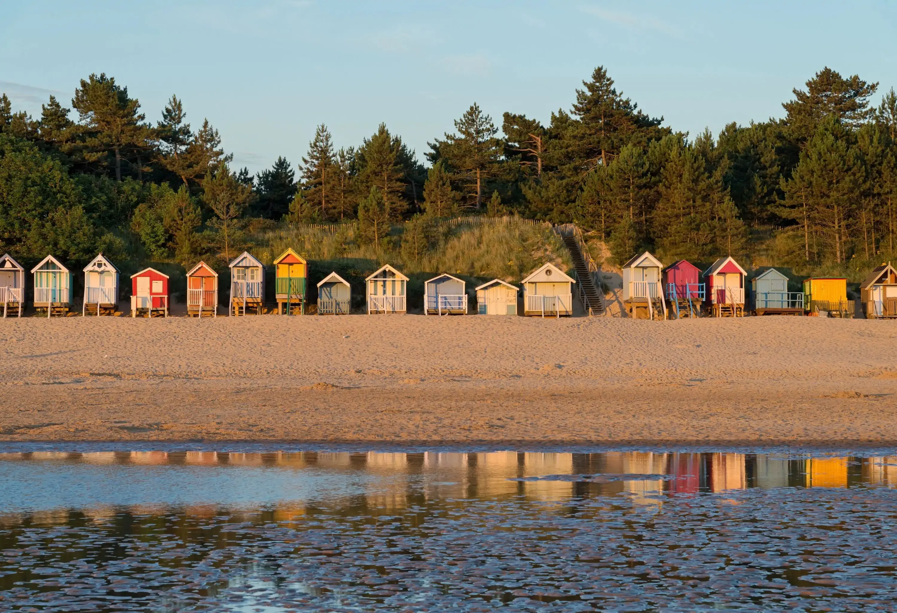 A row of colourful shacks on the beach backed by tall trees.