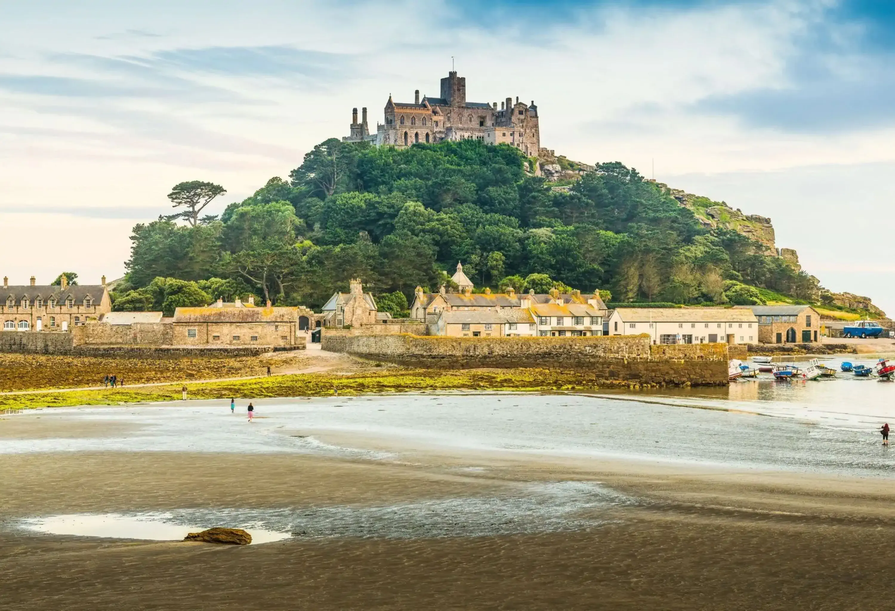 Gentle ocean tide ebbing across the iconic cobbled causeway as warm summer sunlight illuminates the historic chapel, hamlet and harbour of St. Michael's Mount, Marazion, Cornwall, UK.