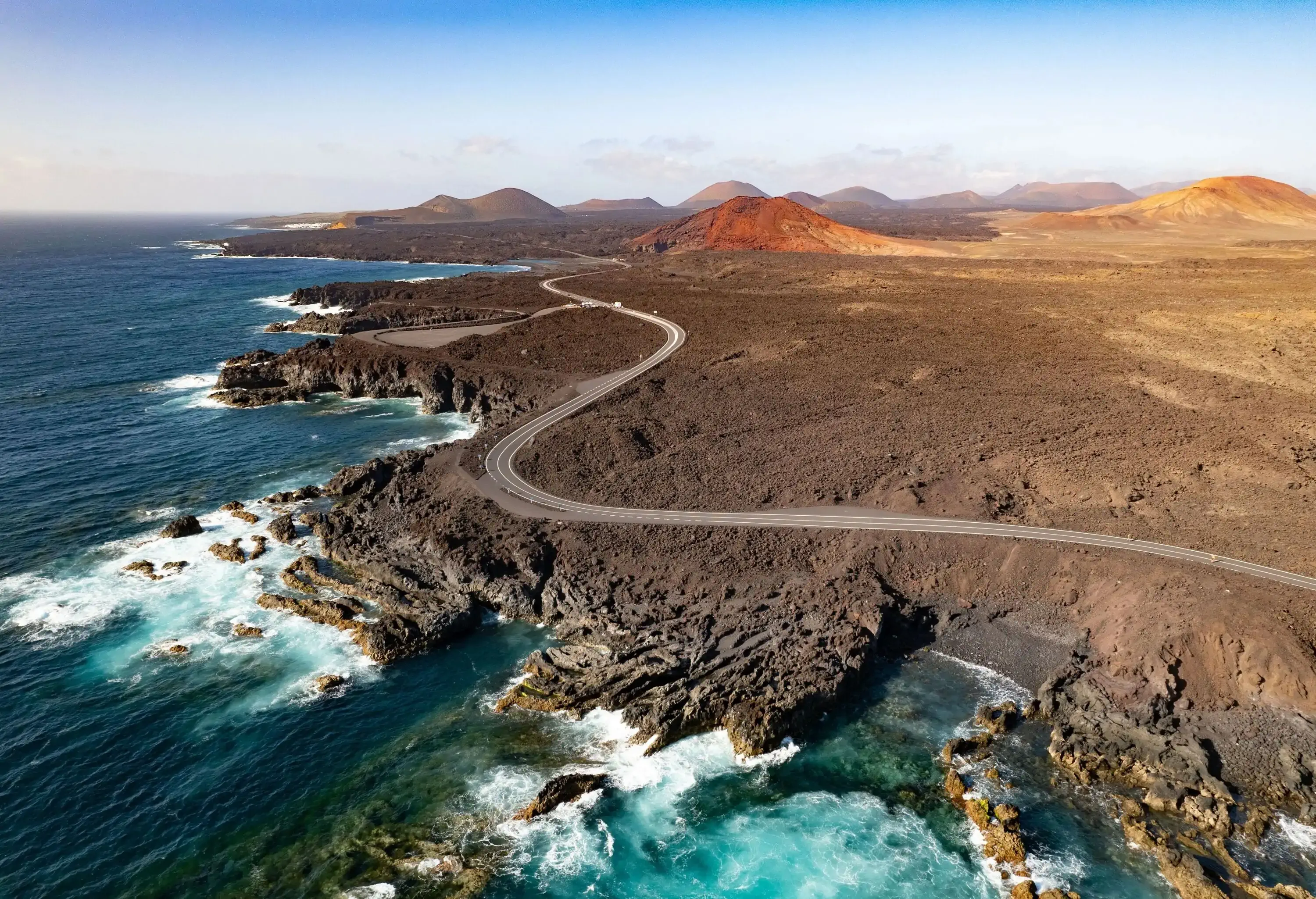 A desolate, winding, long road along the coast with sporadic hills.