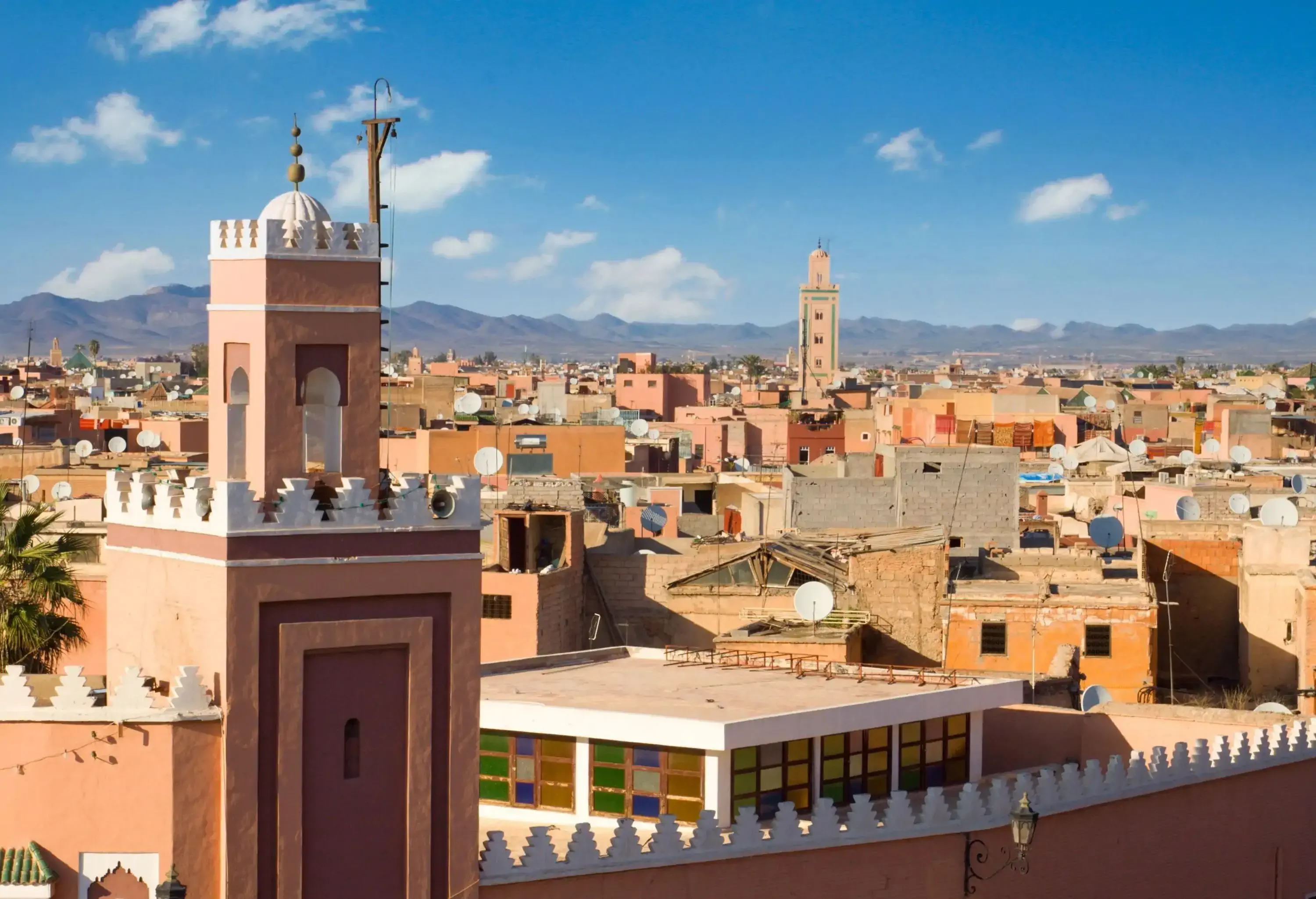 Skyline of a city with traditional brown buildings against the mountain range and the cloudy blue sky.
