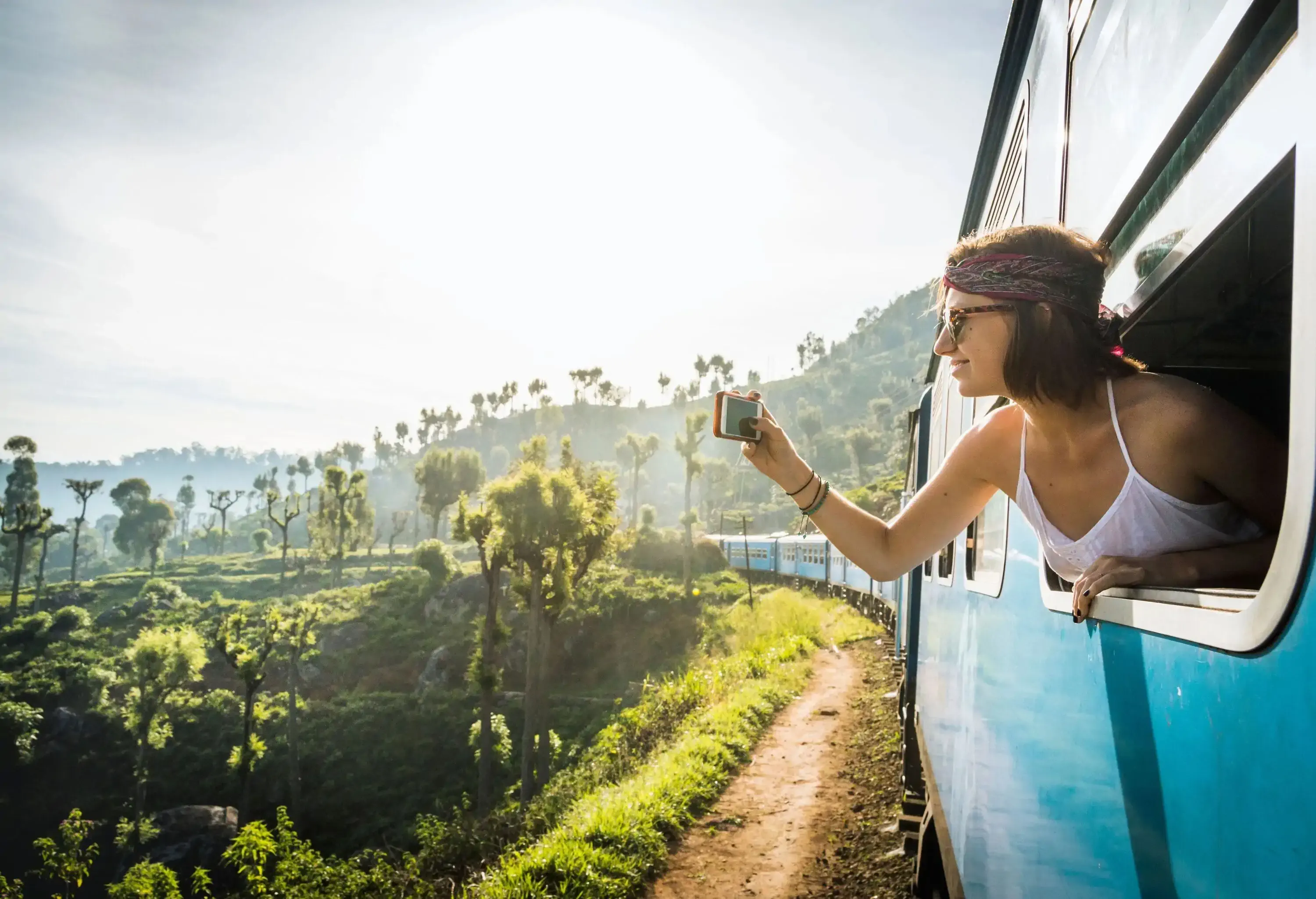 A woman peeking out of a bus window to take a picture of the beautiful scenery.