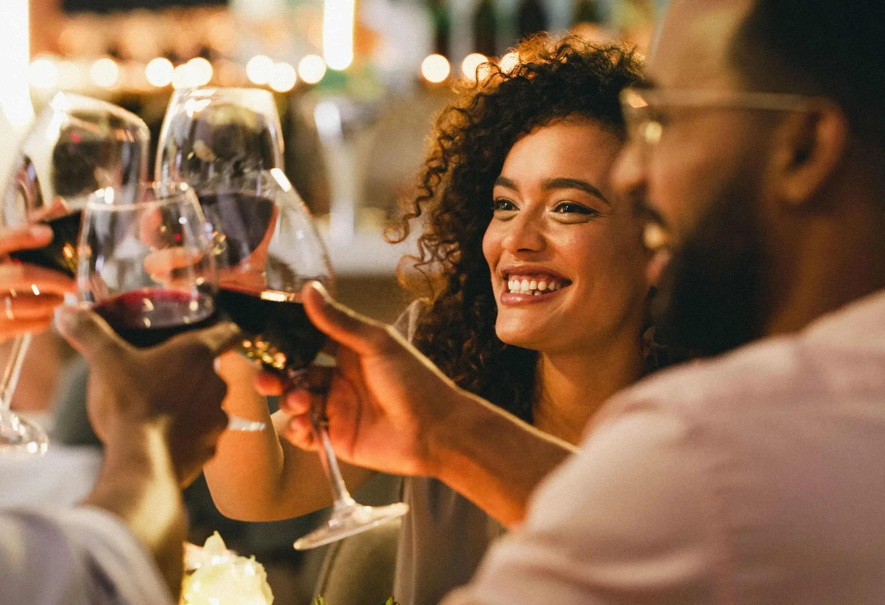A group of cheerful and lively young friends raise their glasses in a toast, their smiles reflecting the joy and camaraderie of the moment.