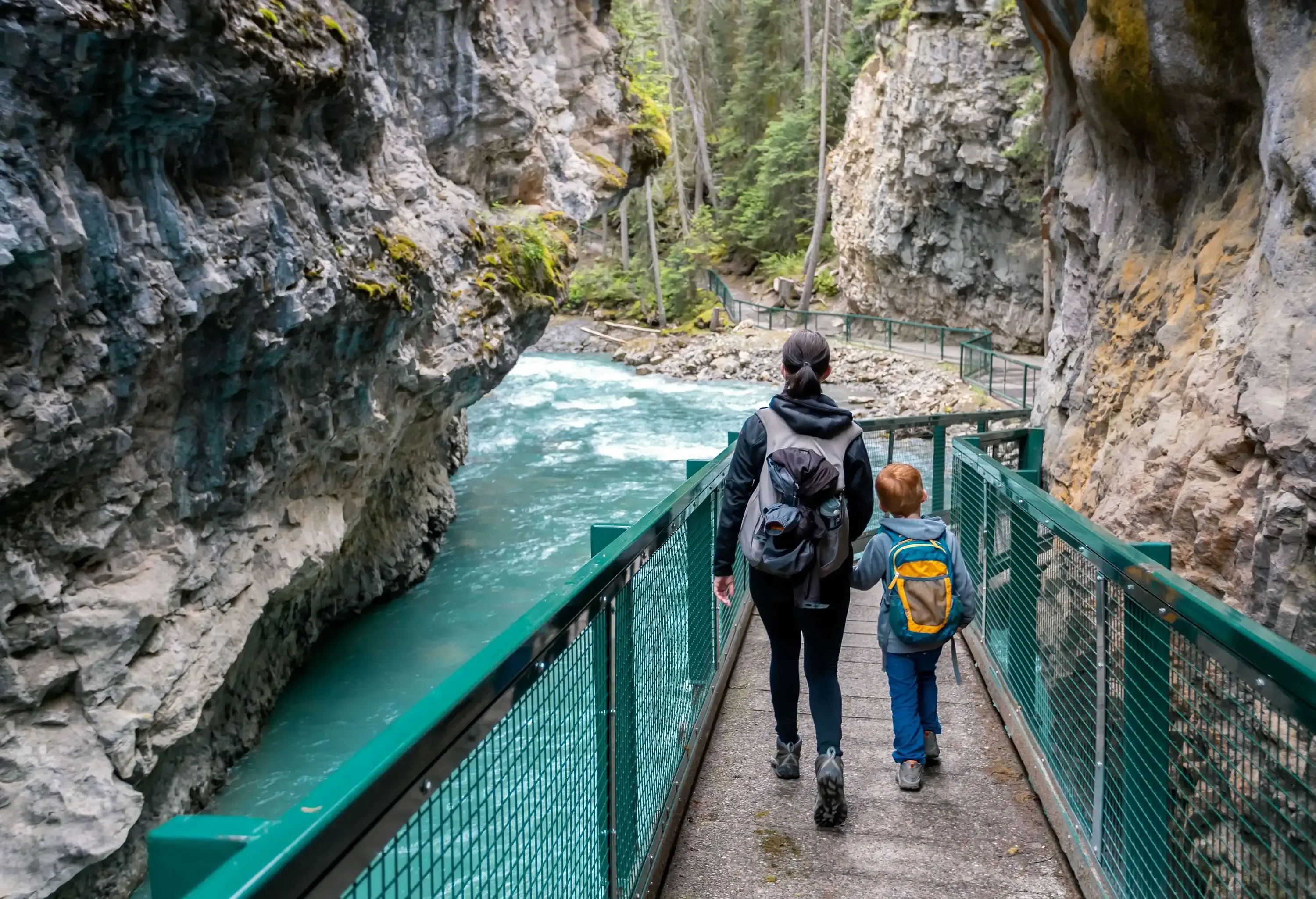 A mother and son strolling down a fenced footbridge across a river between rock gorges.