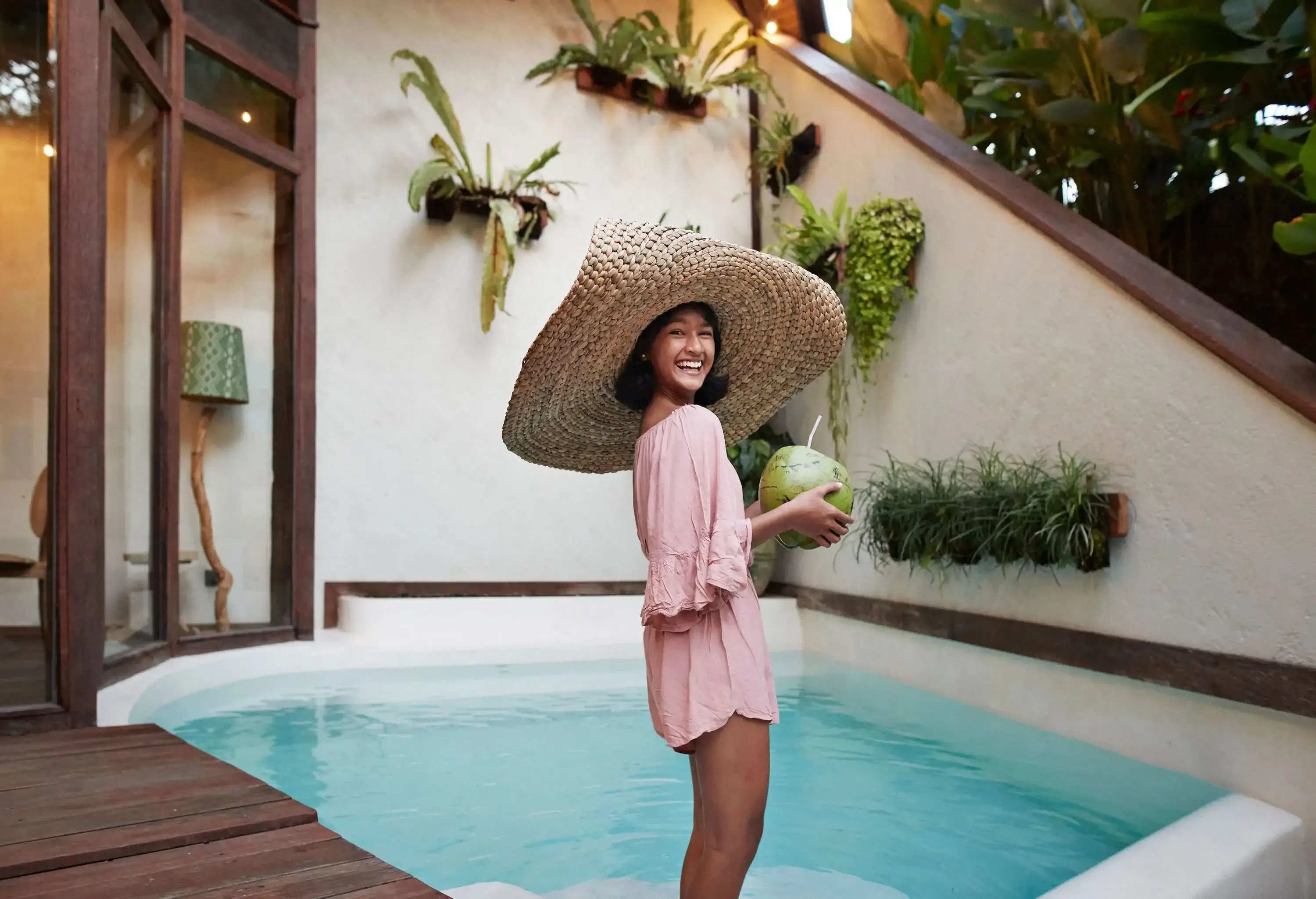 Side view portrait of woman wearing large straw hat while standing near pool at resort during vacation