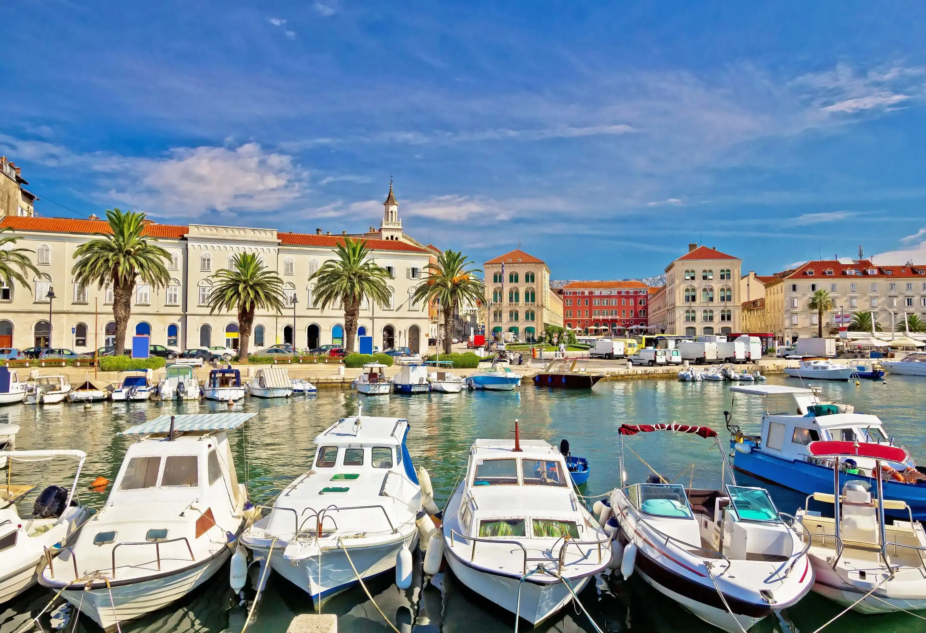 Boats moored in the marina lined with classic buildings against the cloudy blue sky.