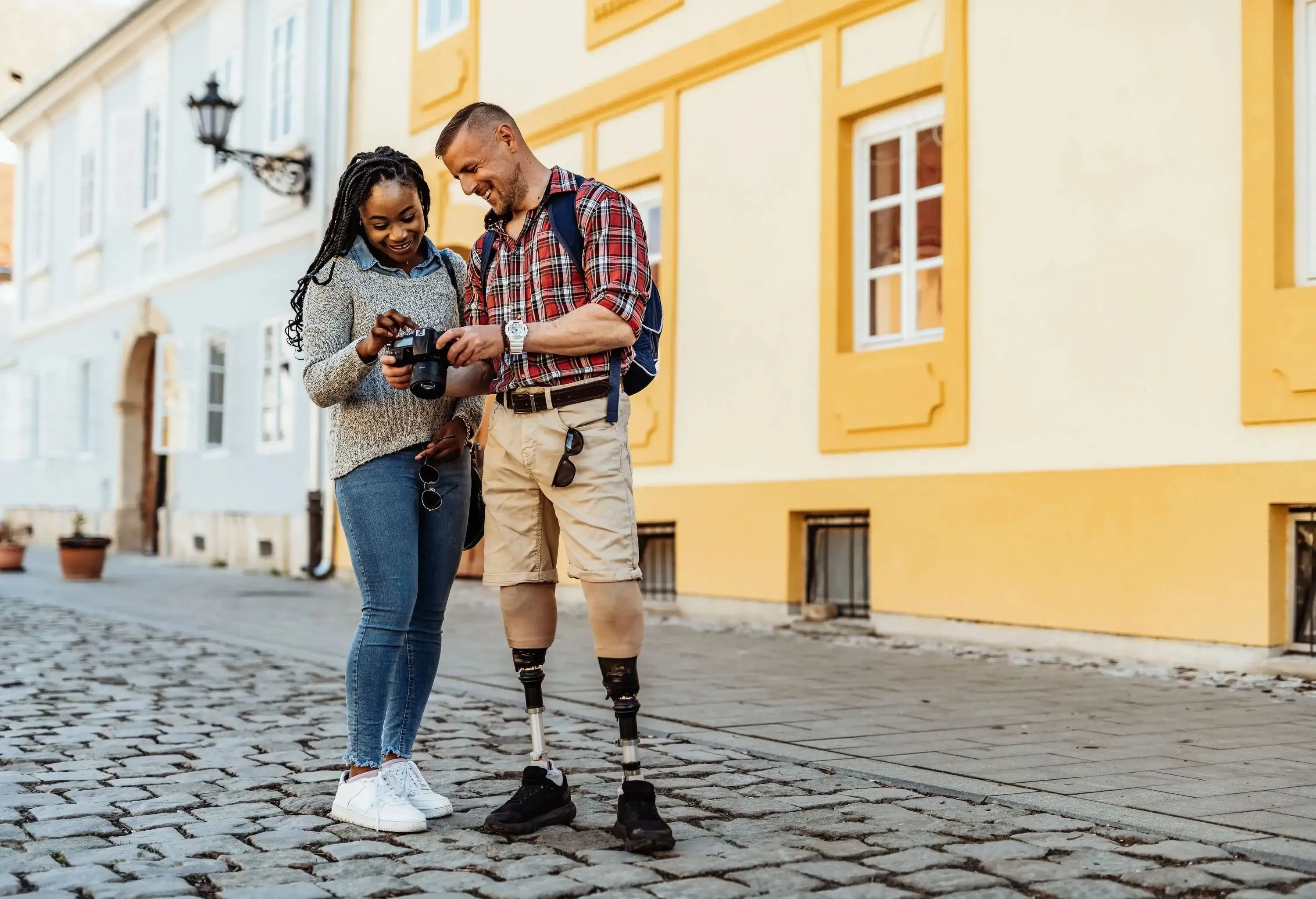 A woman and a man with prosthetic legs standing on a pavement while checking on their digital camera.