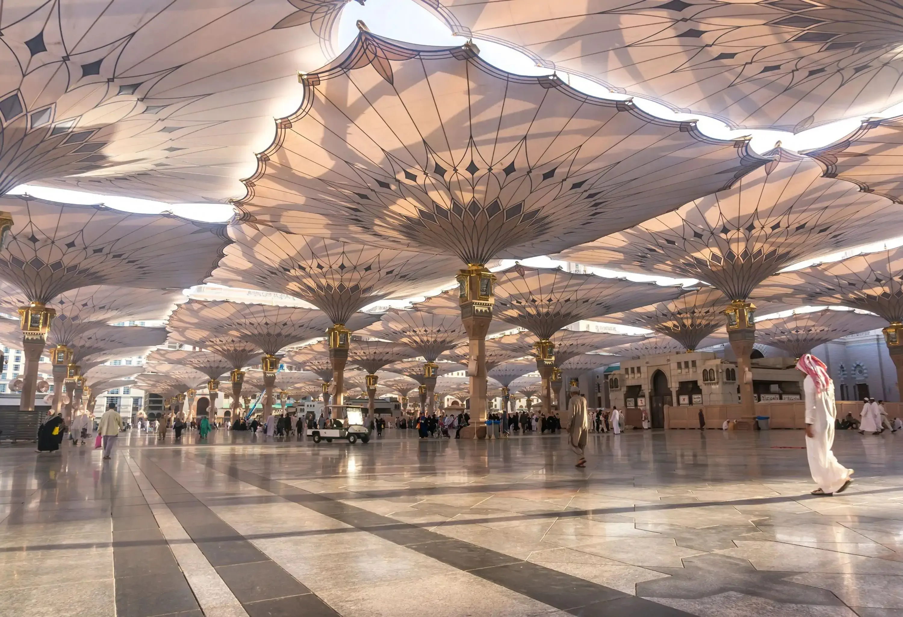 People walking across the tiled floor of a courtyard covered with fluted-edged decorative sun shades.