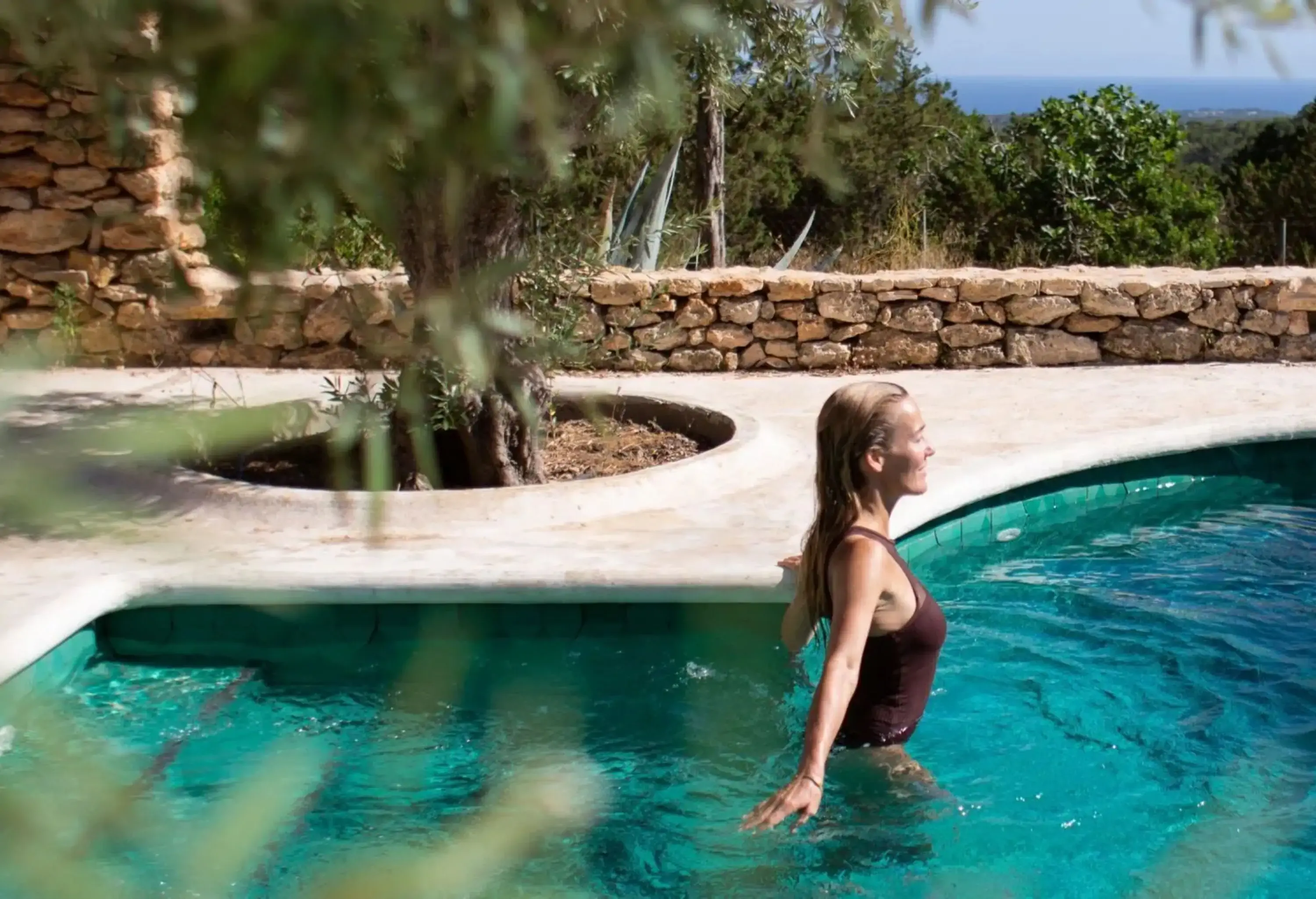 Woman going for a swim in outdoor pool with the sea in the background