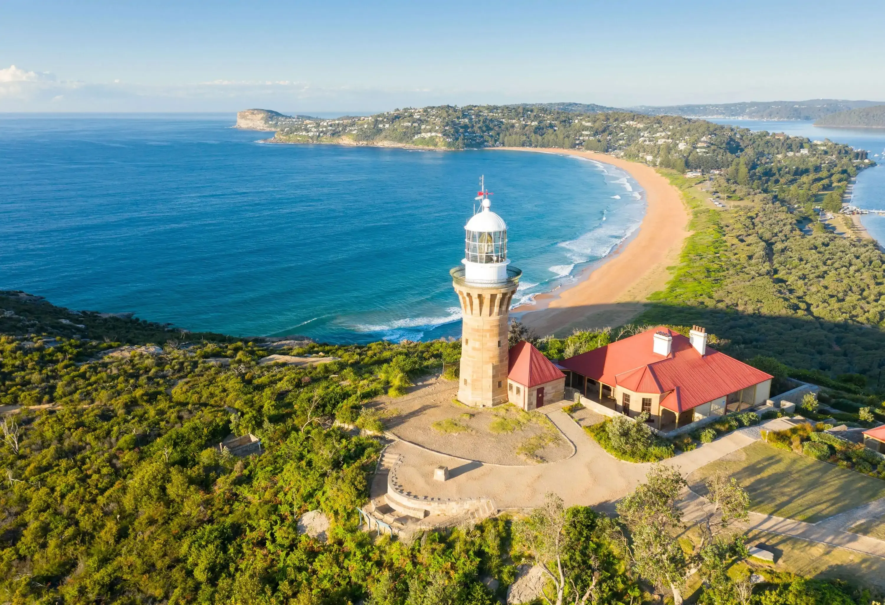 A stately lighthouse stands sentinel beside an accompanying building, both overlooking the vast sea and enveloped by verdant trees.
