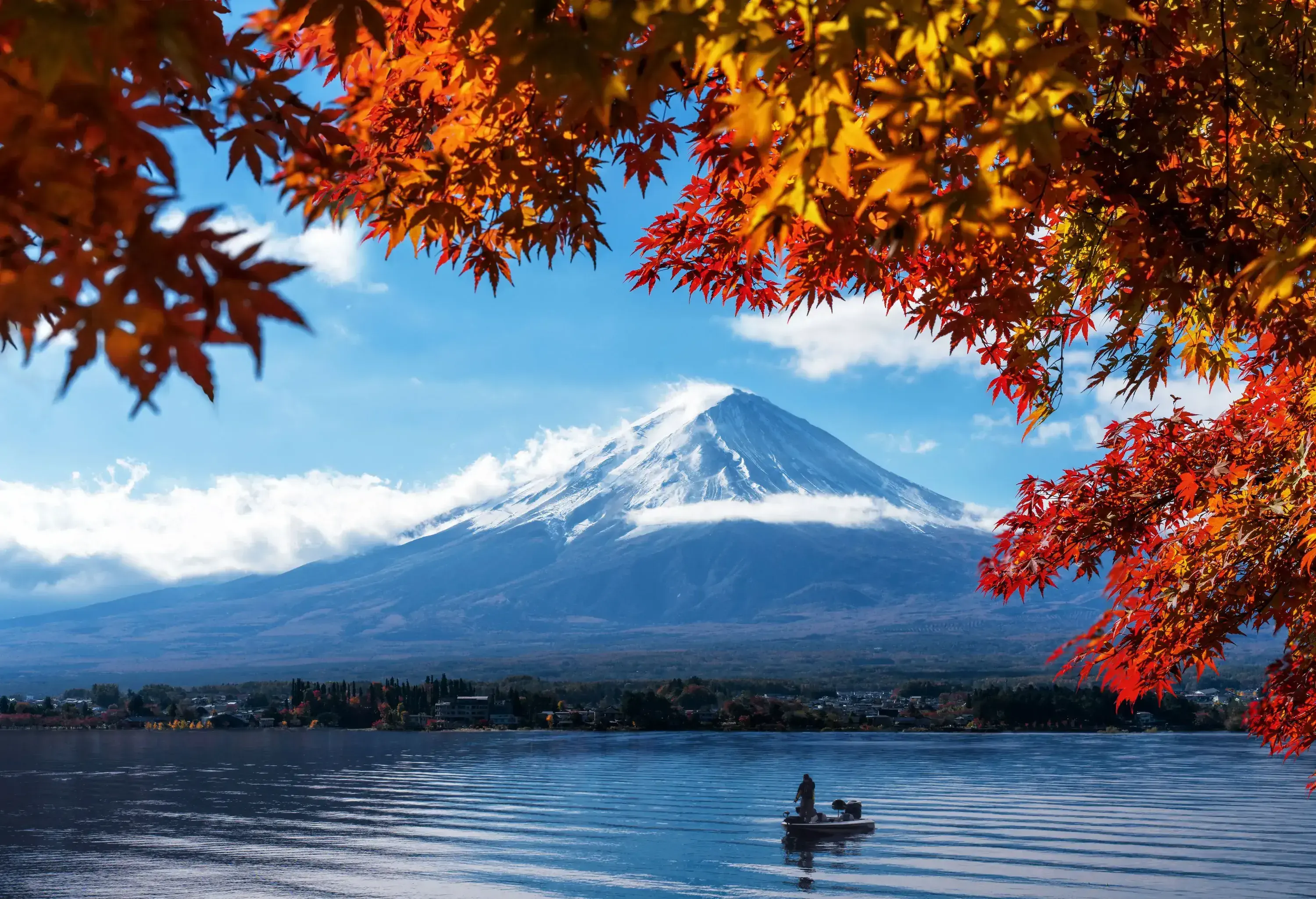 A person on a boat floating across a lake in front of the majestic Mount Fuji.