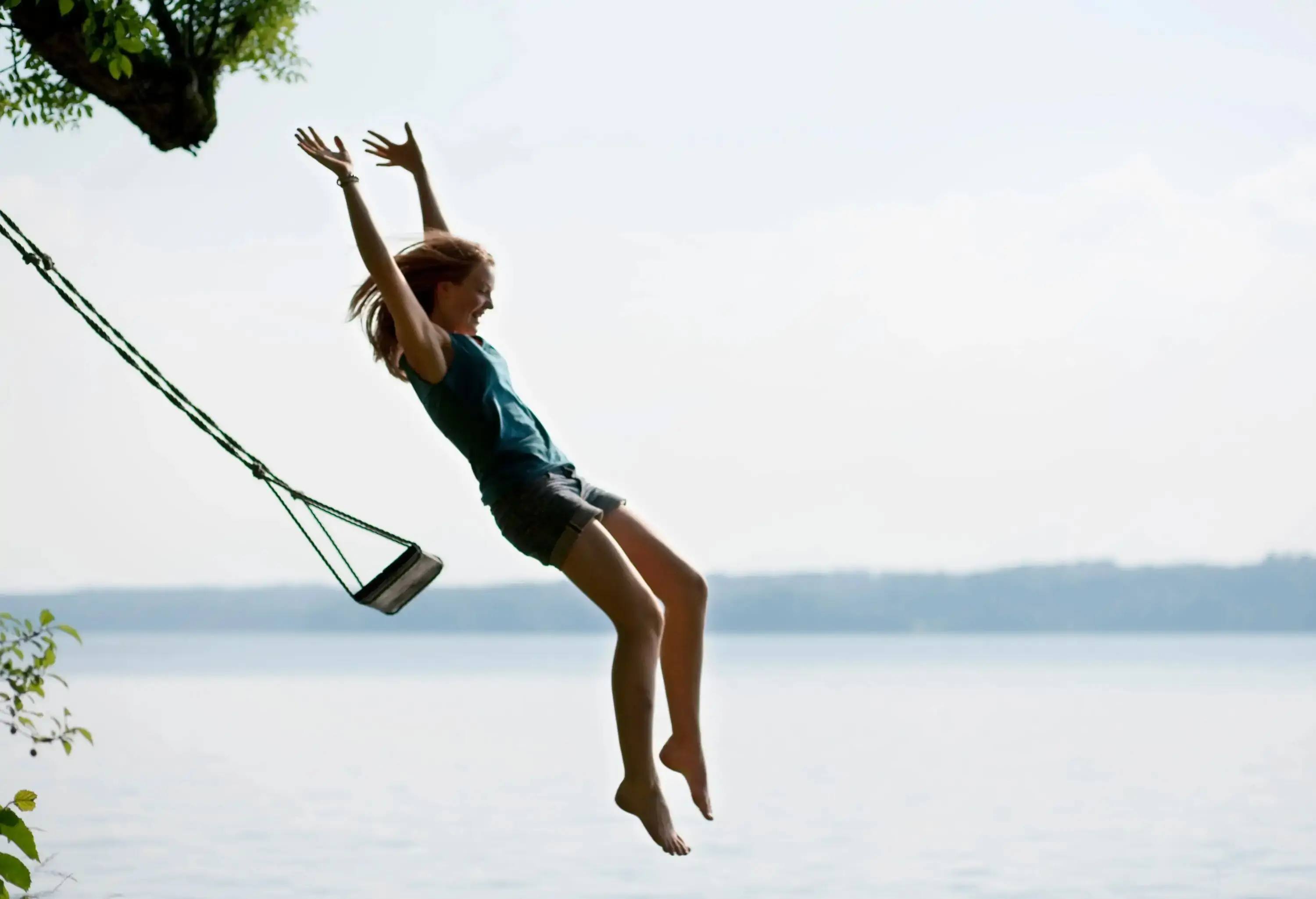A young girl jumping off a swing into the water.