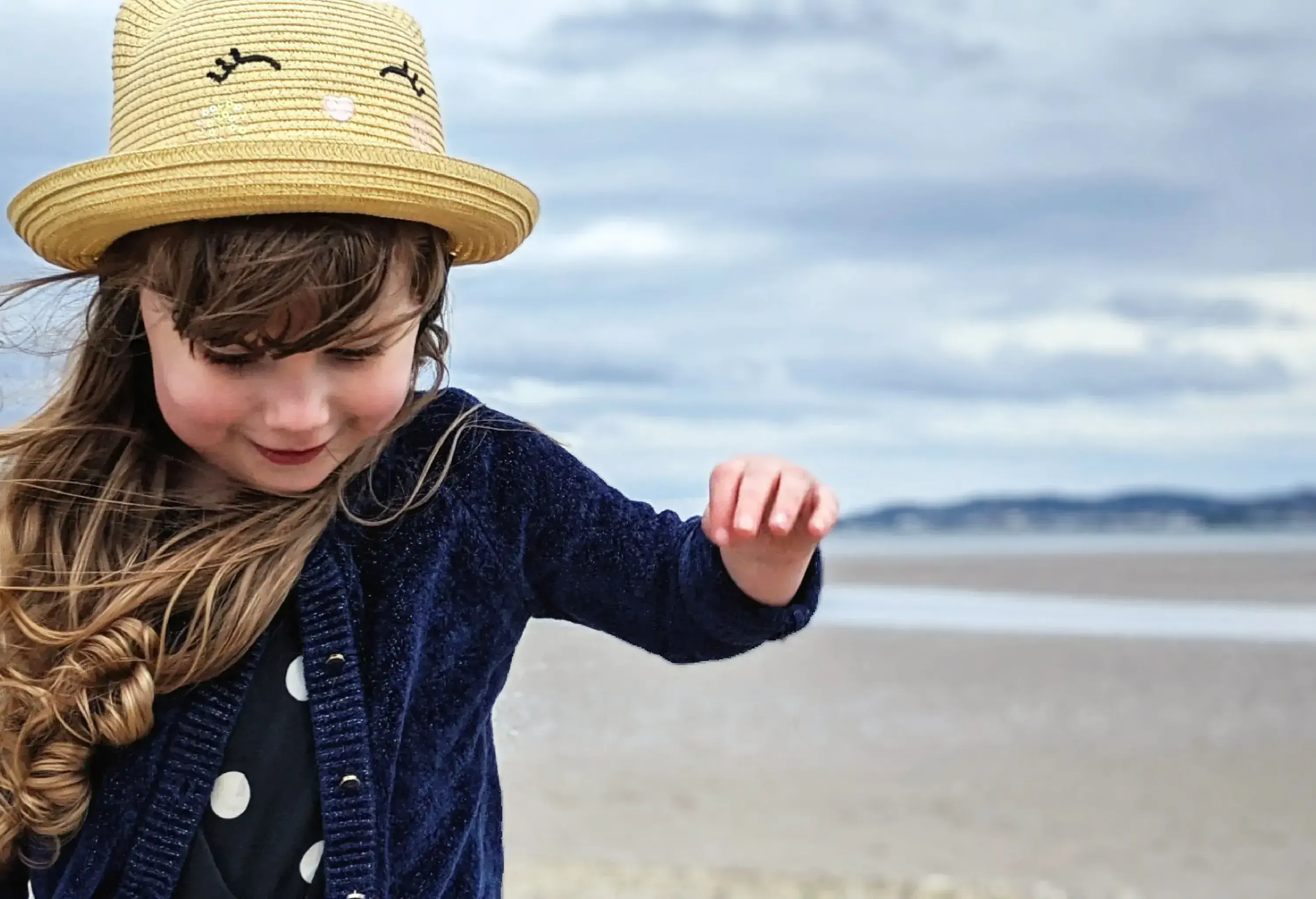 A brunette girl in a straw hat smiles and looks down.