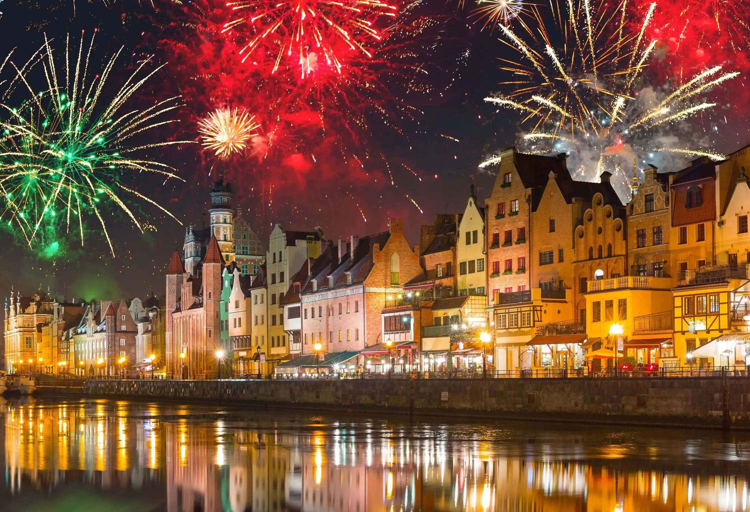 Fireworks bursting in a rainbow of colours over the buildings alongside a canal.