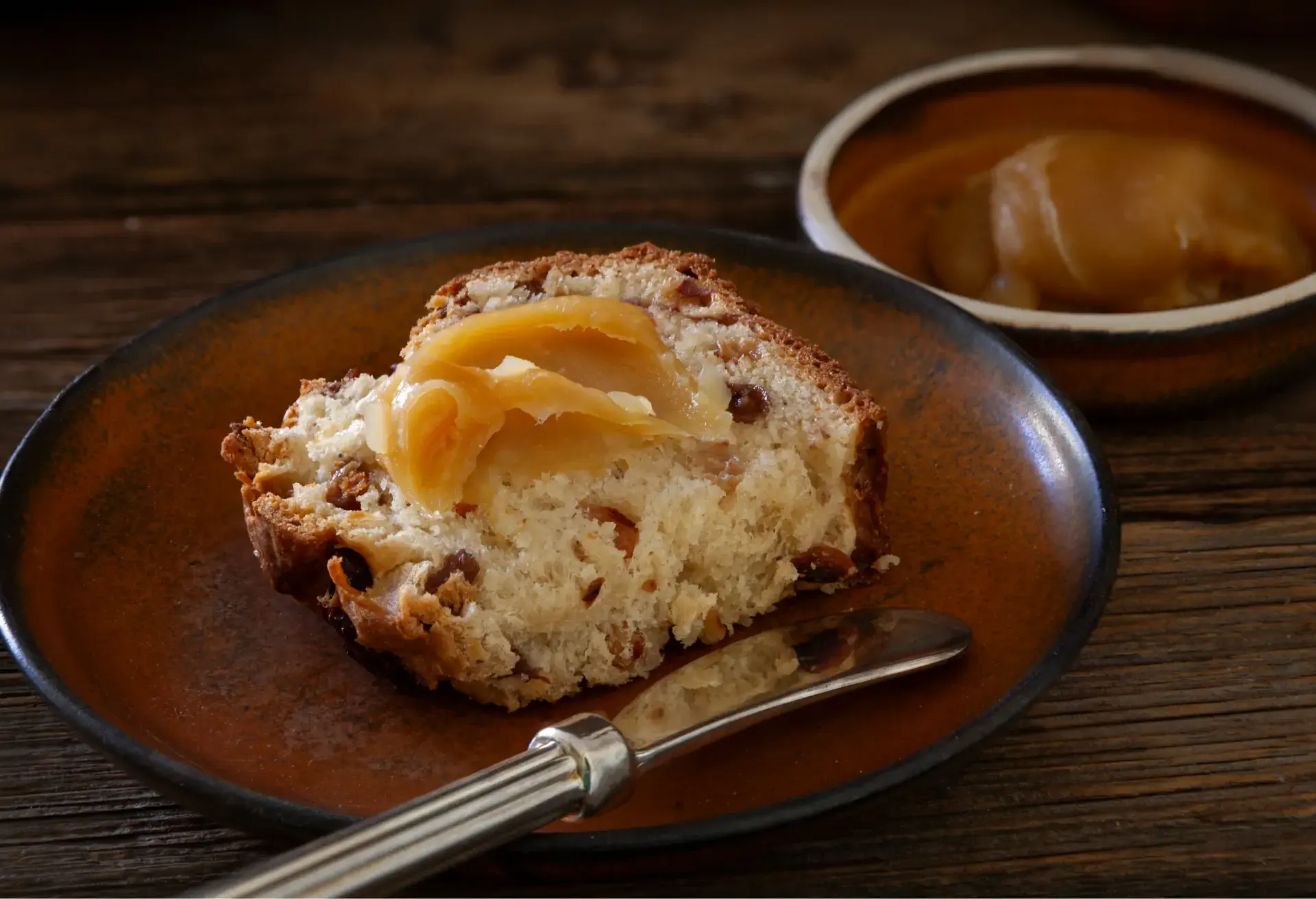 Slice of barmbrack fruit bread topped with butter on a brown plate.