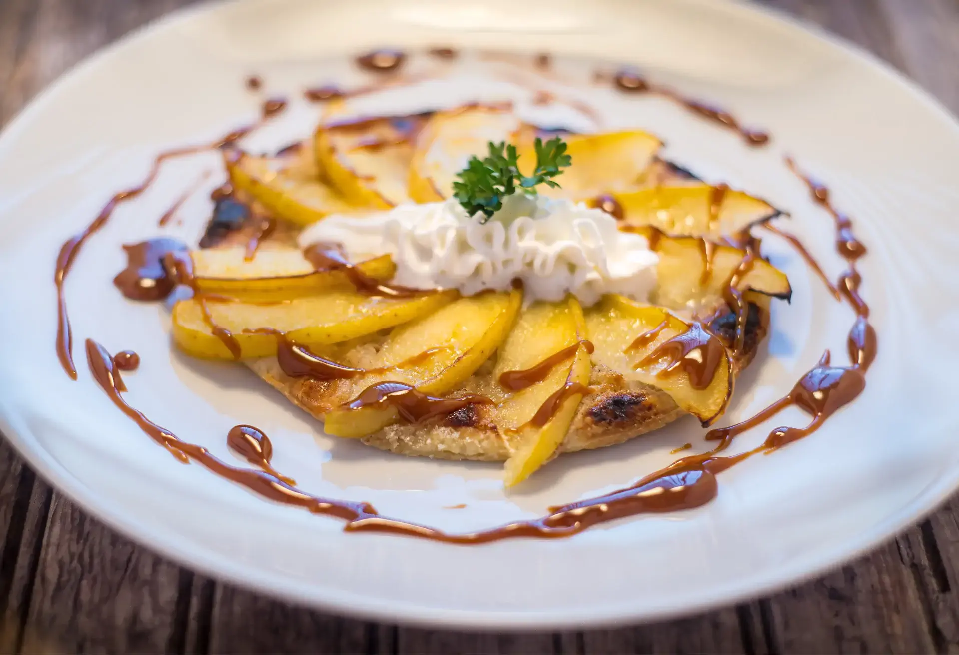 Apple tart drizzled with caramel sauce and topped with whipped cream and parsley.