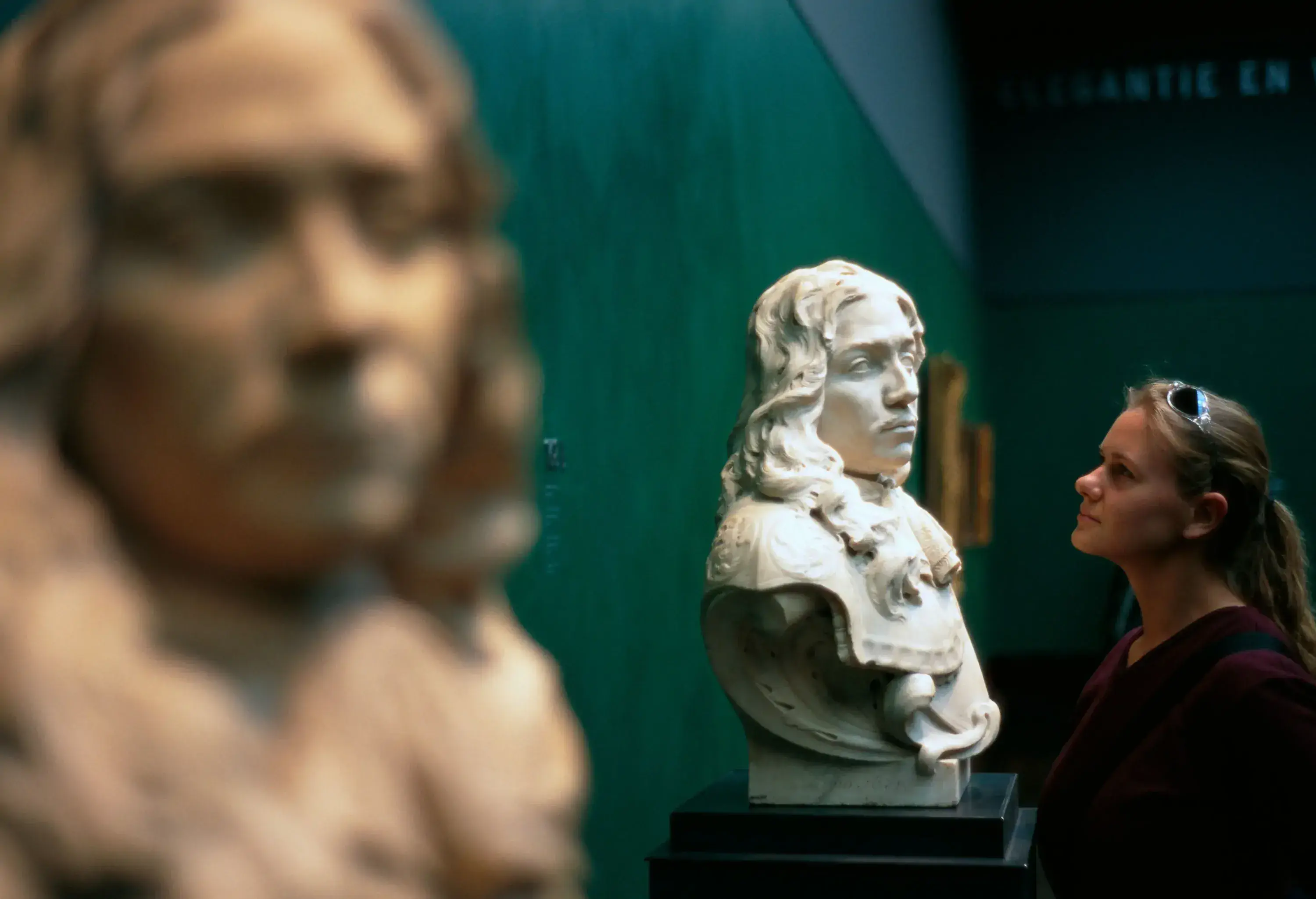 A person admires a bust sculpture, captivated by its details, as it stands out against a dimly lit background.