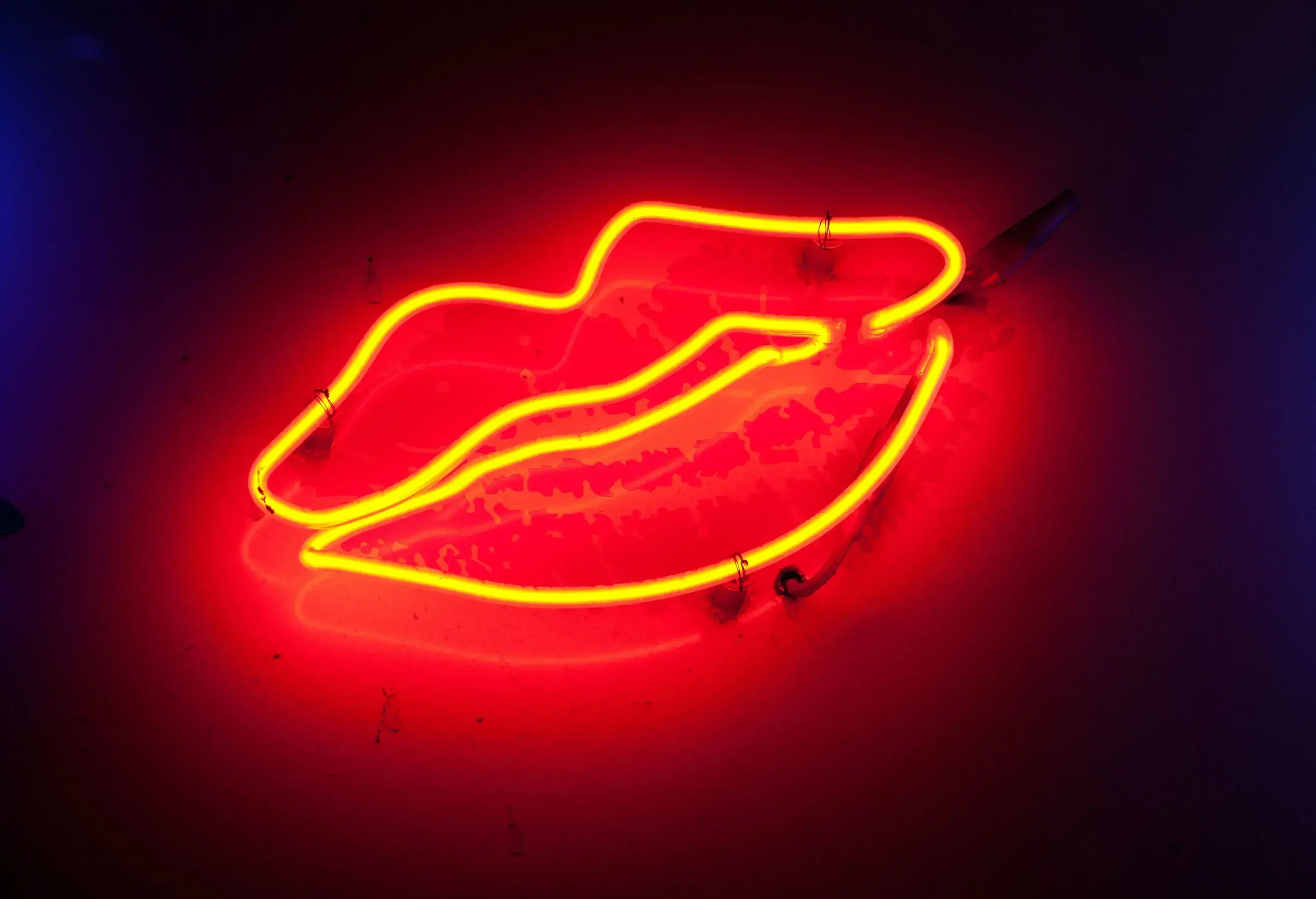 A yellow neon light shaped into a lip hung on a red wall.