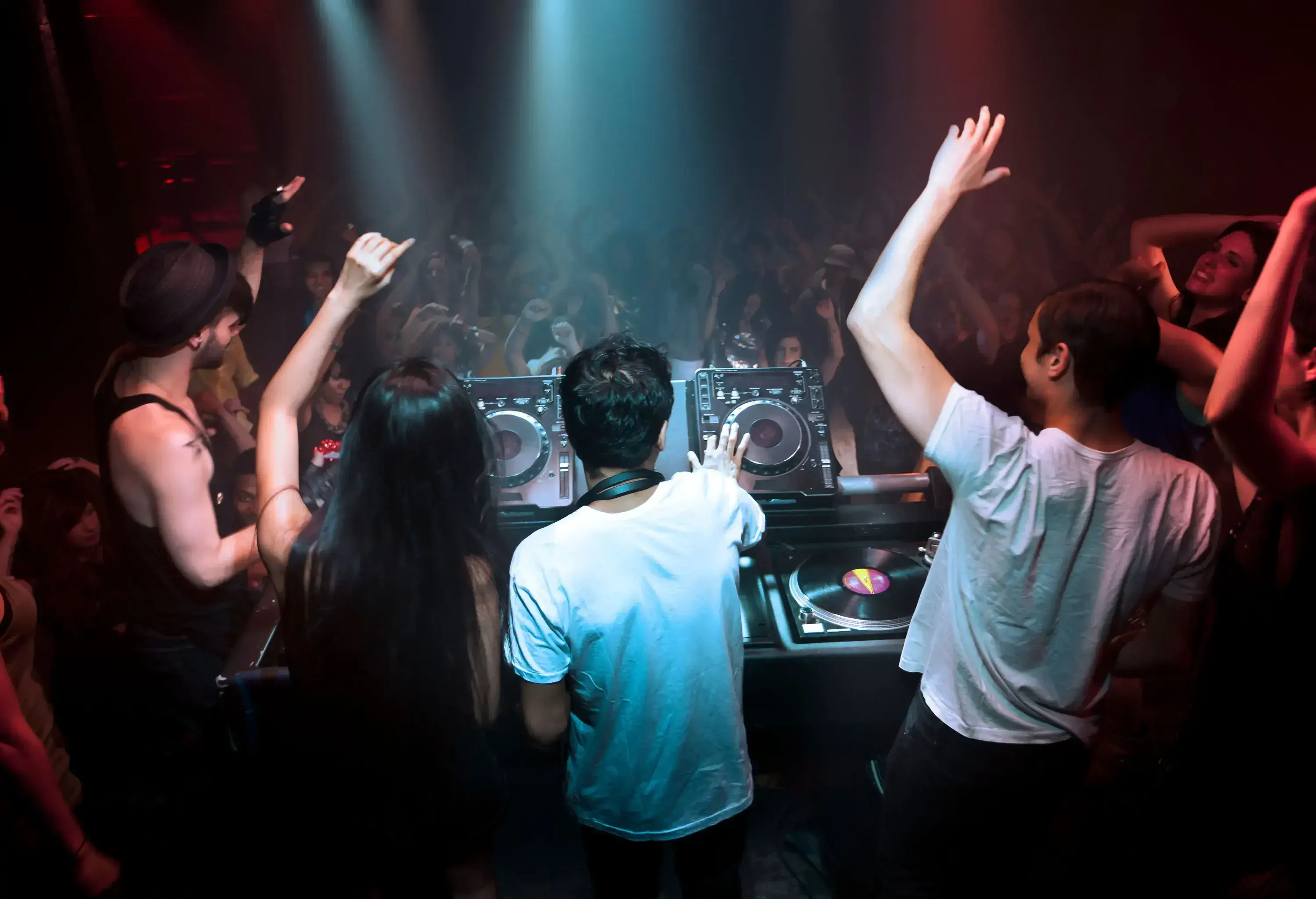 A DJ plays music using a controller inside a crowded nightclub.