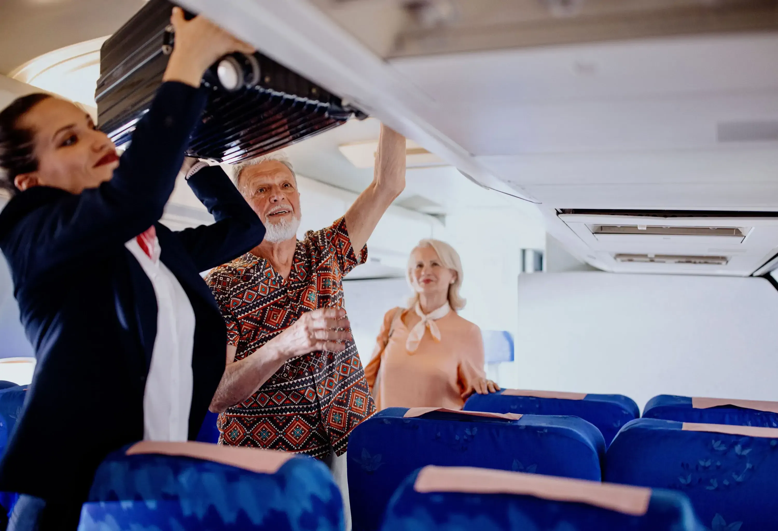Cabin Crew helps passenger with putting bags and suitcases in overhead locker