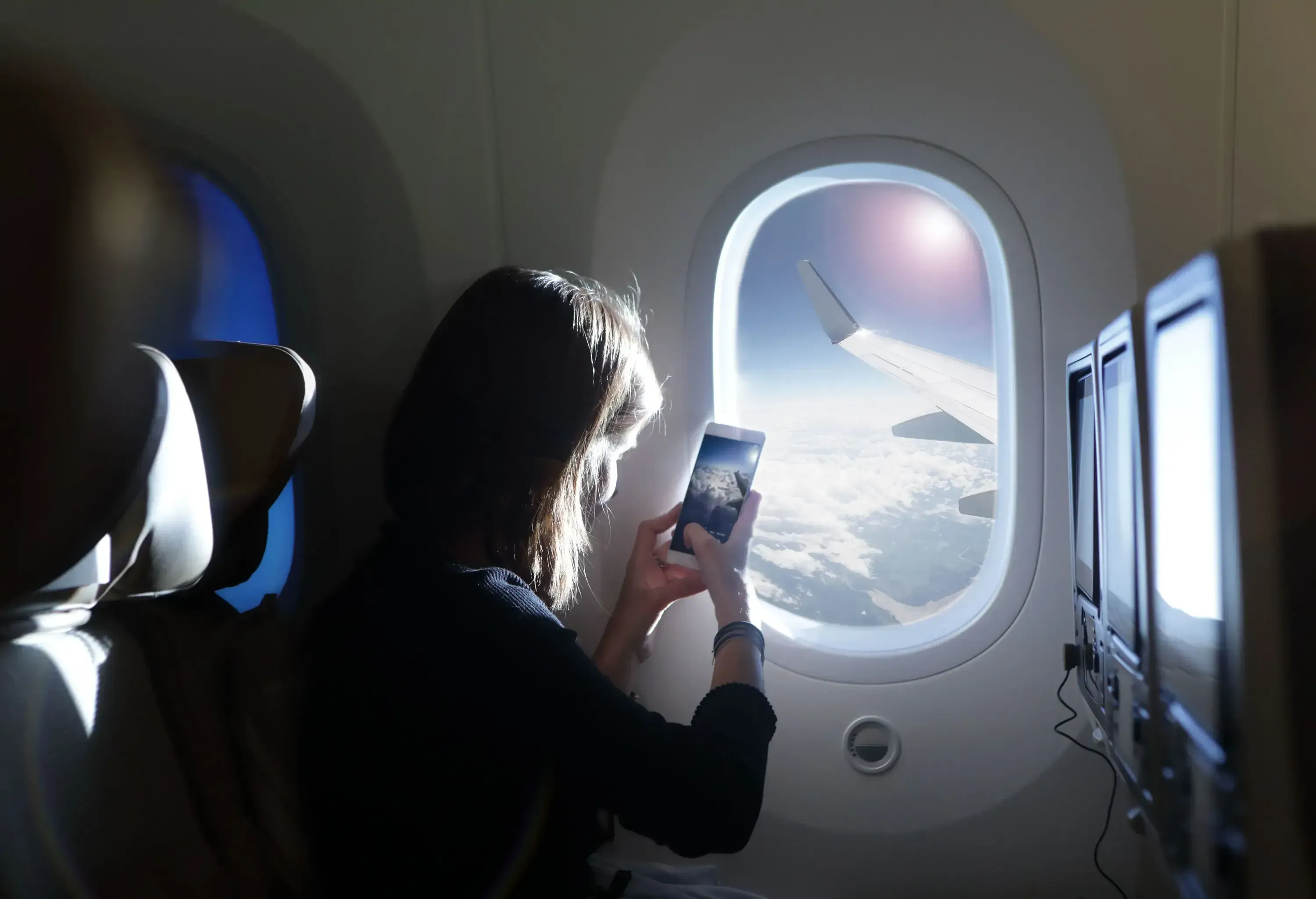 A young girl taking a picture of the view outside the airplane window with her smartphone.