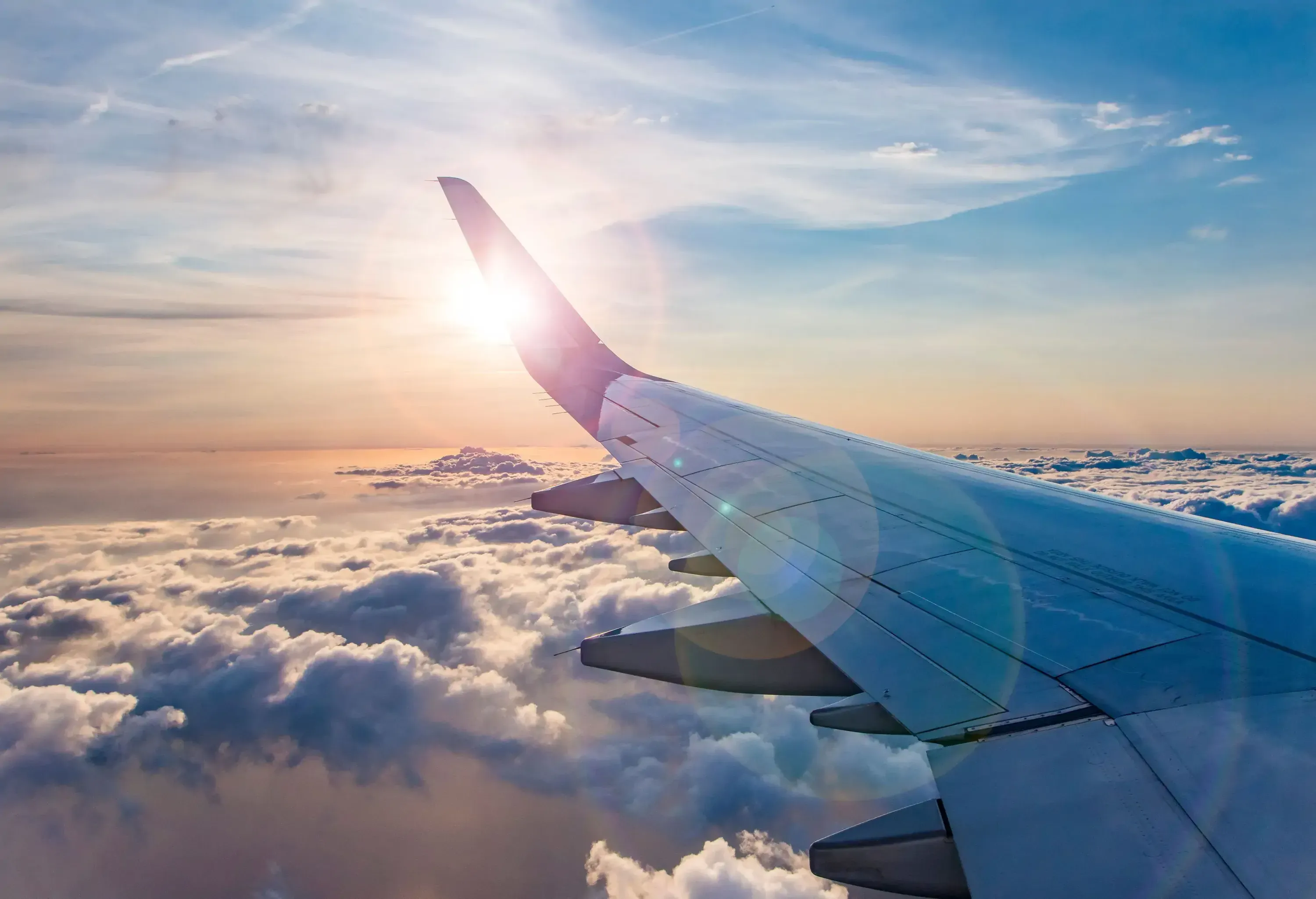 The sun peeks through the wing of an airplane flying above the clouds.