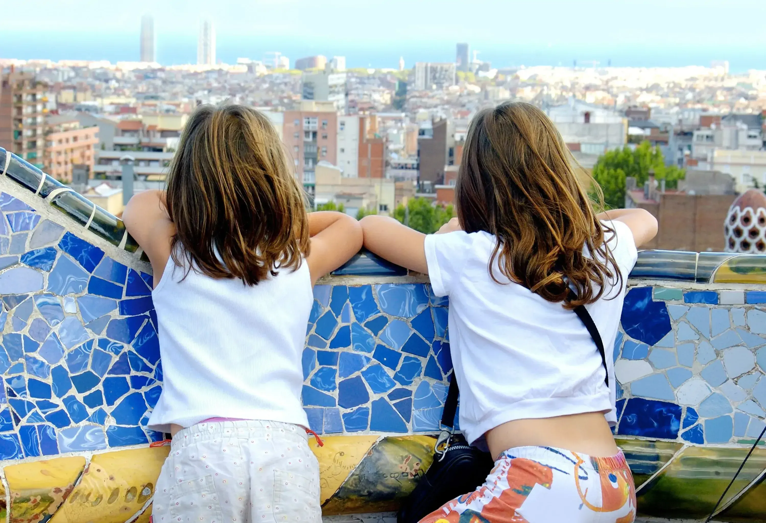 Two kids gaze at the cityscape with their arms placed on the ledge of a colourful bench.