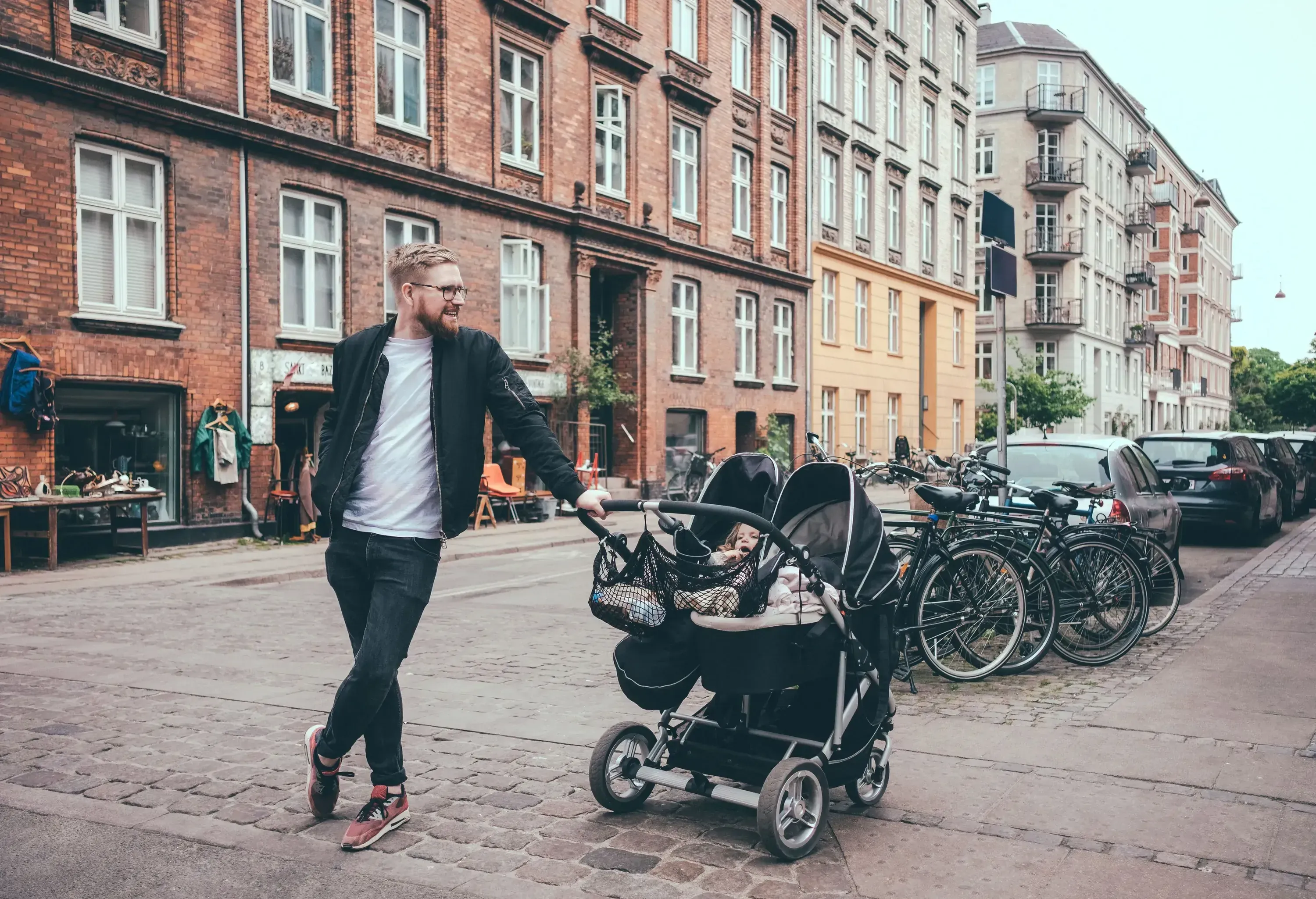 A man leaning on a double stroller as he stands on the side of the road.