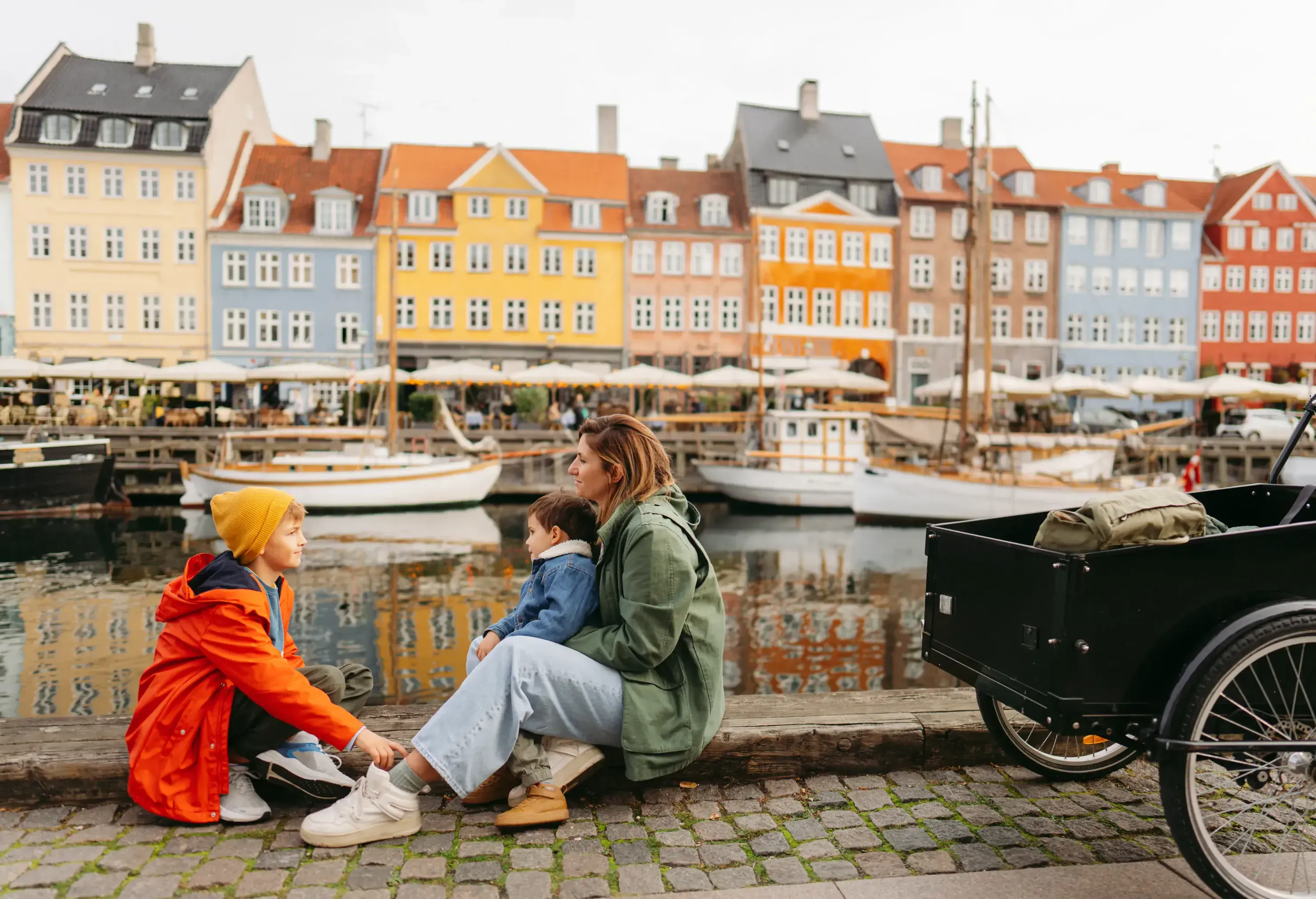 Photo of a young mom with two boys enjoy the view of colourful traditional houses in Nyhavn pier, Copenhagen, Denmark.