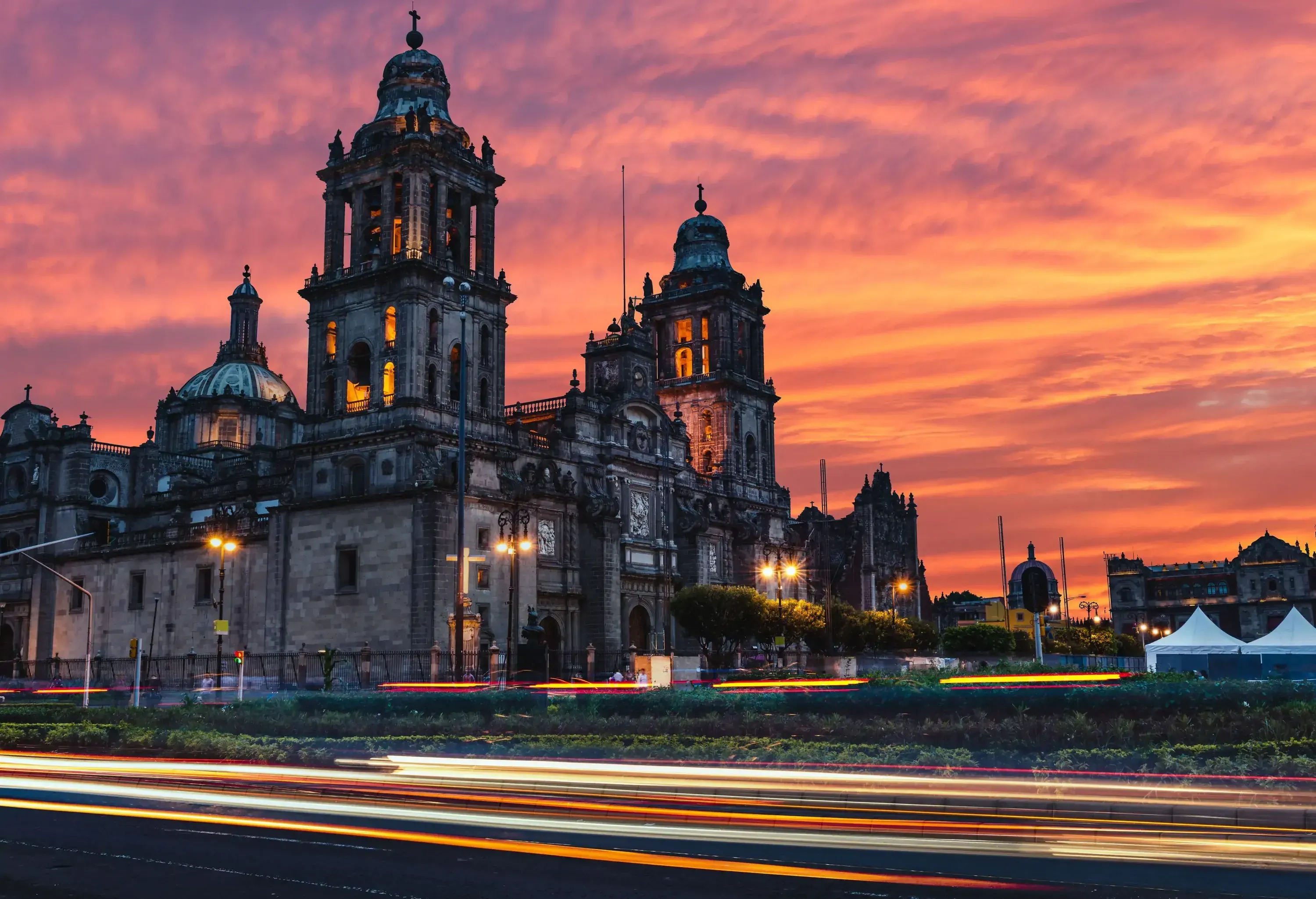 The Mexico City Metropolitan Cathedral, a magnificent edifice boasting intricate baroque and neoclassical exteriors, adorned with ornate stone carvings, towering bell towers, and a grand central dome, stands majestic under the soft glow of the sunrise.