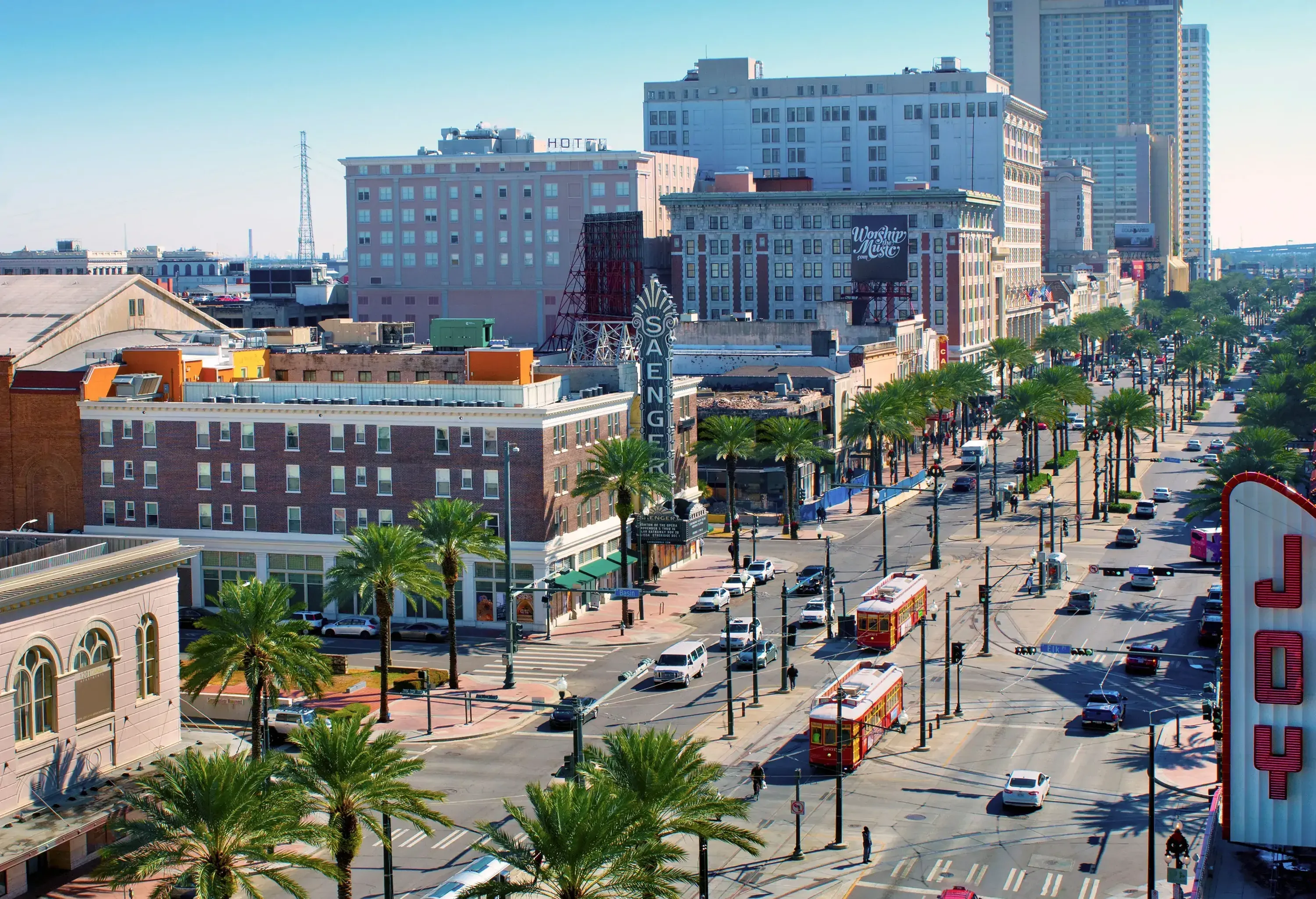 Two trams on a tramway in the middle of a two-lane highway bordered by city buildings.