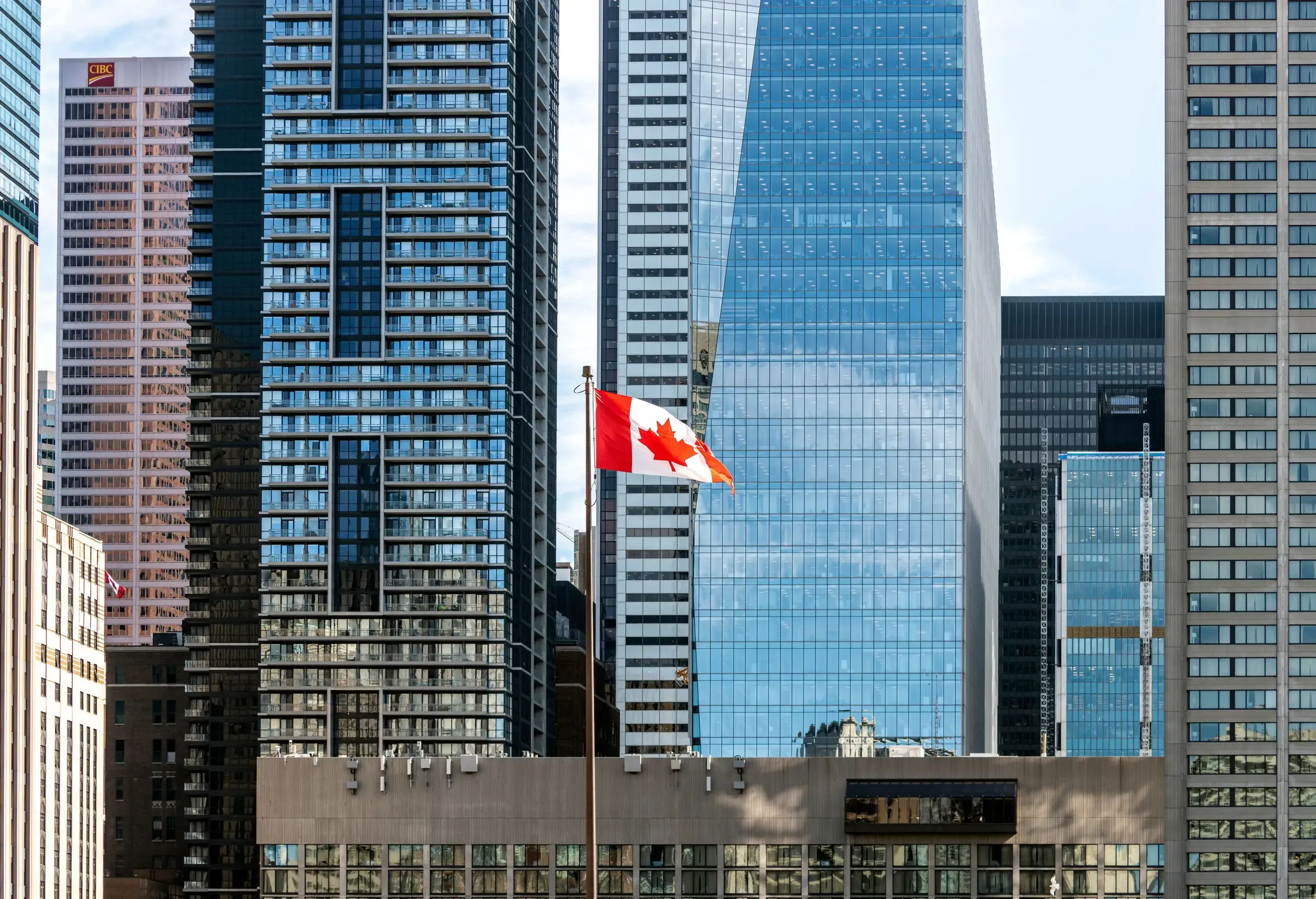 A proud Canadian flag billows in the breeze, with towering skyscrapers providing a striking backdrop.