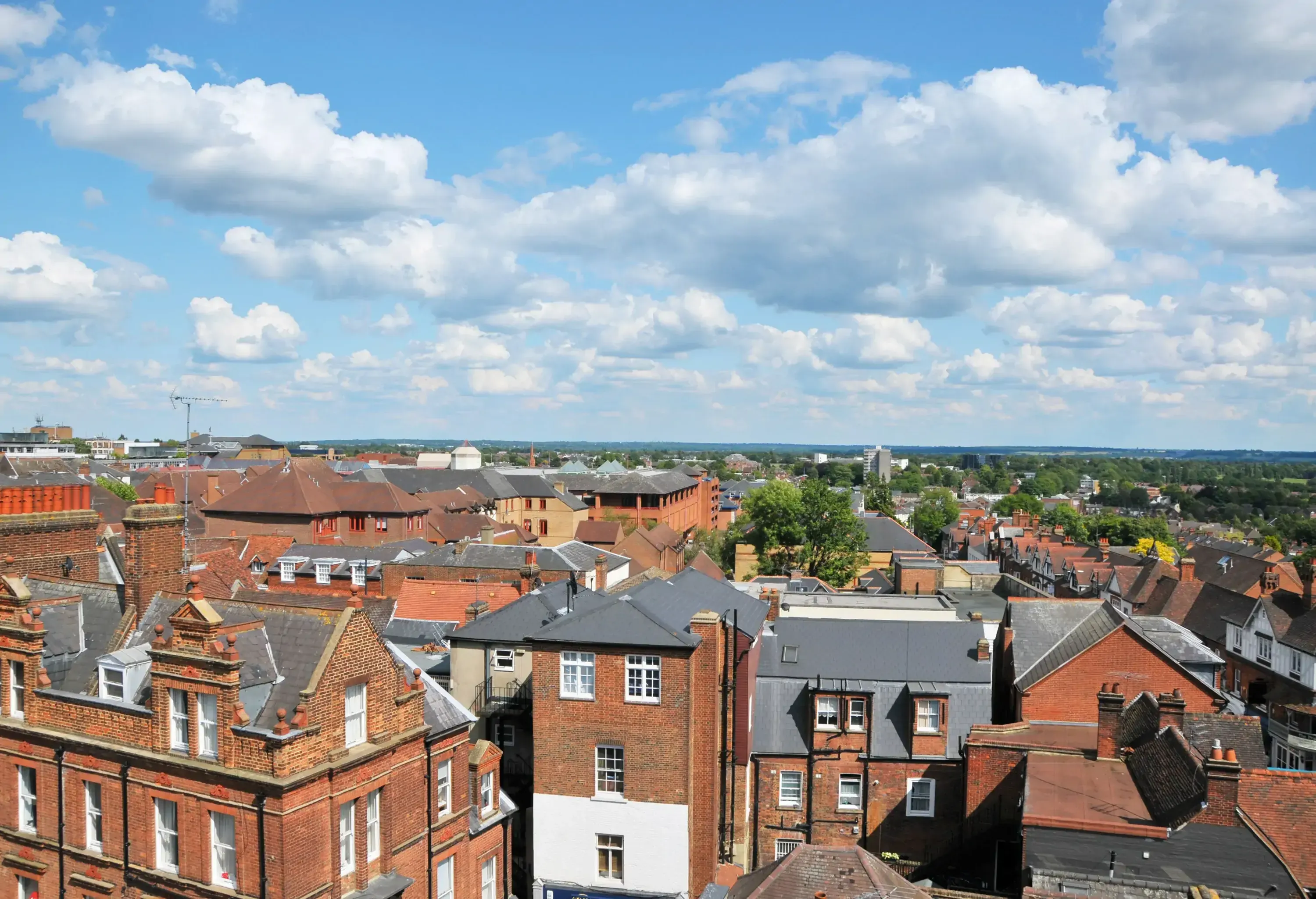 A panoramic view of tall building roofs under a cloudy blue sky.
