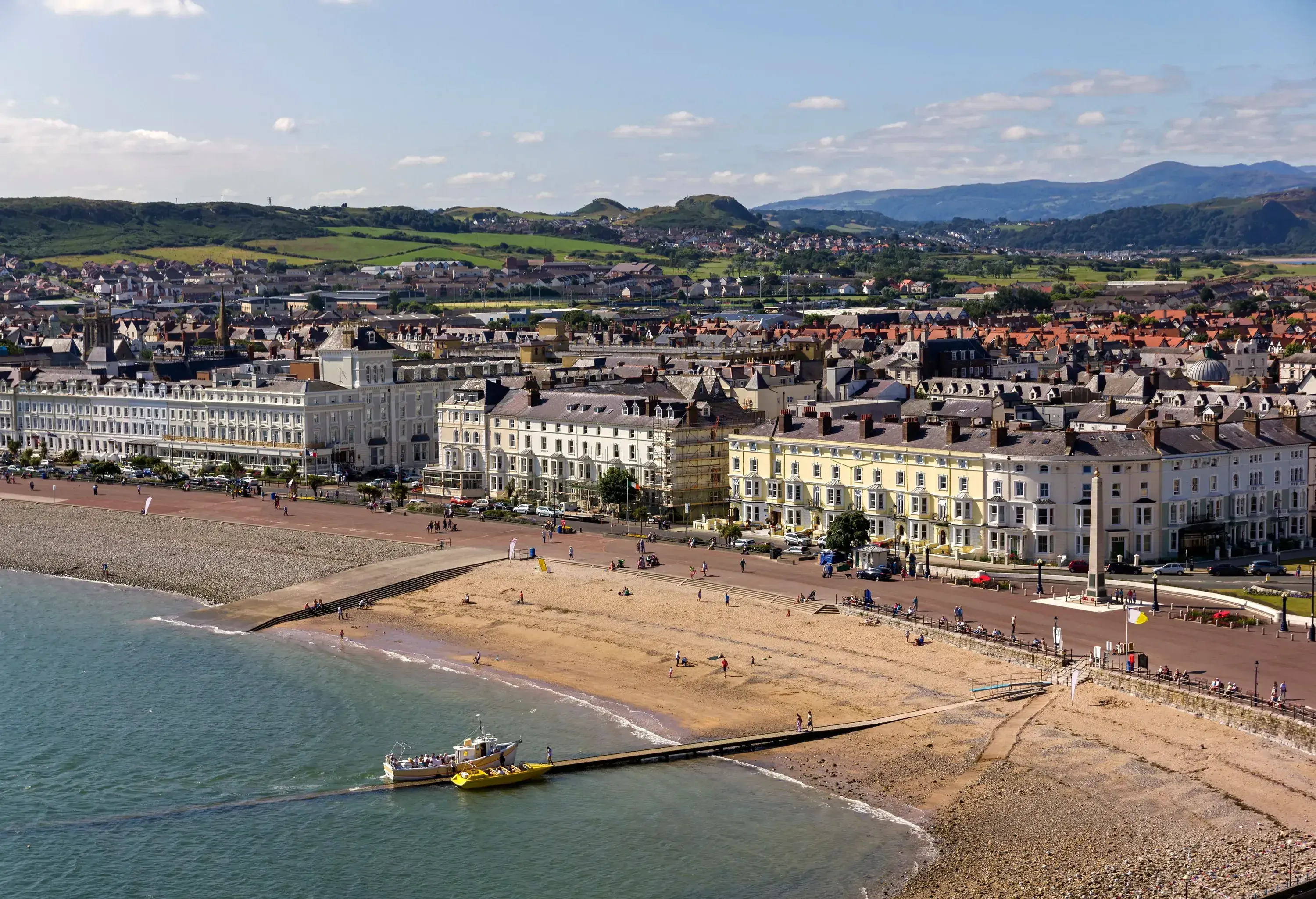 Several people are on the promenade bordering the beach and the cluster of coastal buildings.