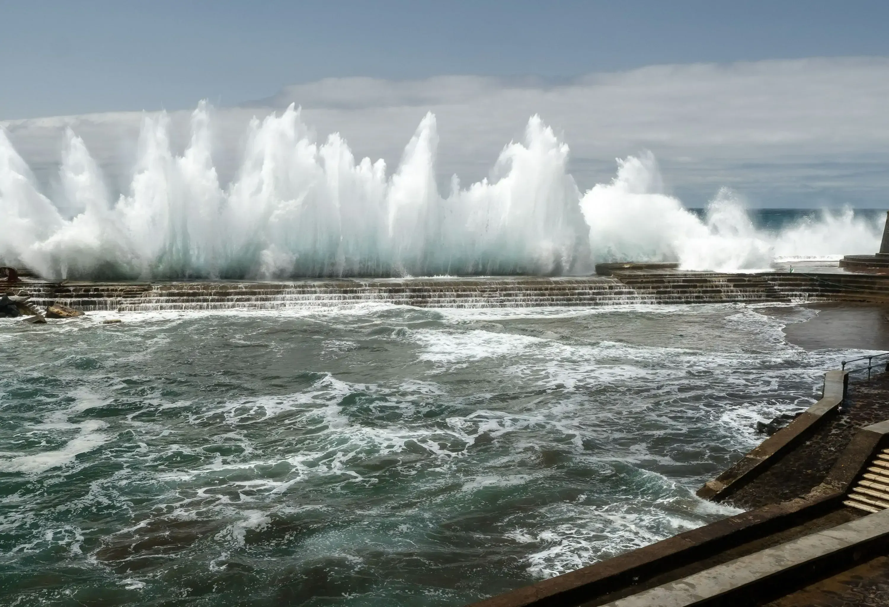 Big waves crashing hard against the breakwater and flooding into an ocean pool.