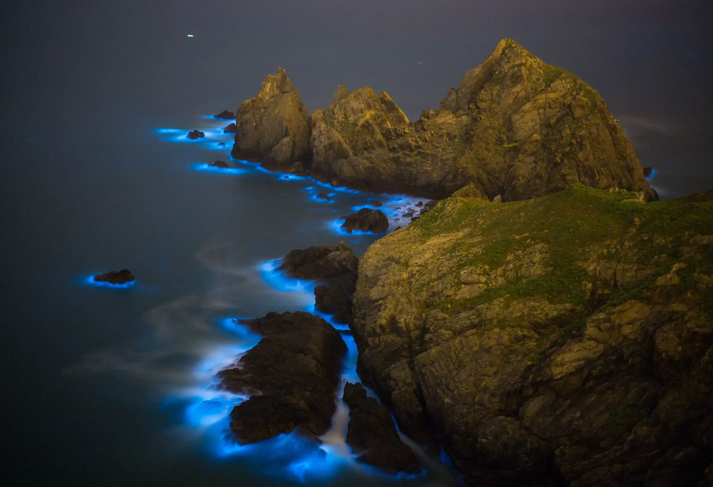 A chain of sea cliffs across the sea outlined with luminescent blue glow at night.
