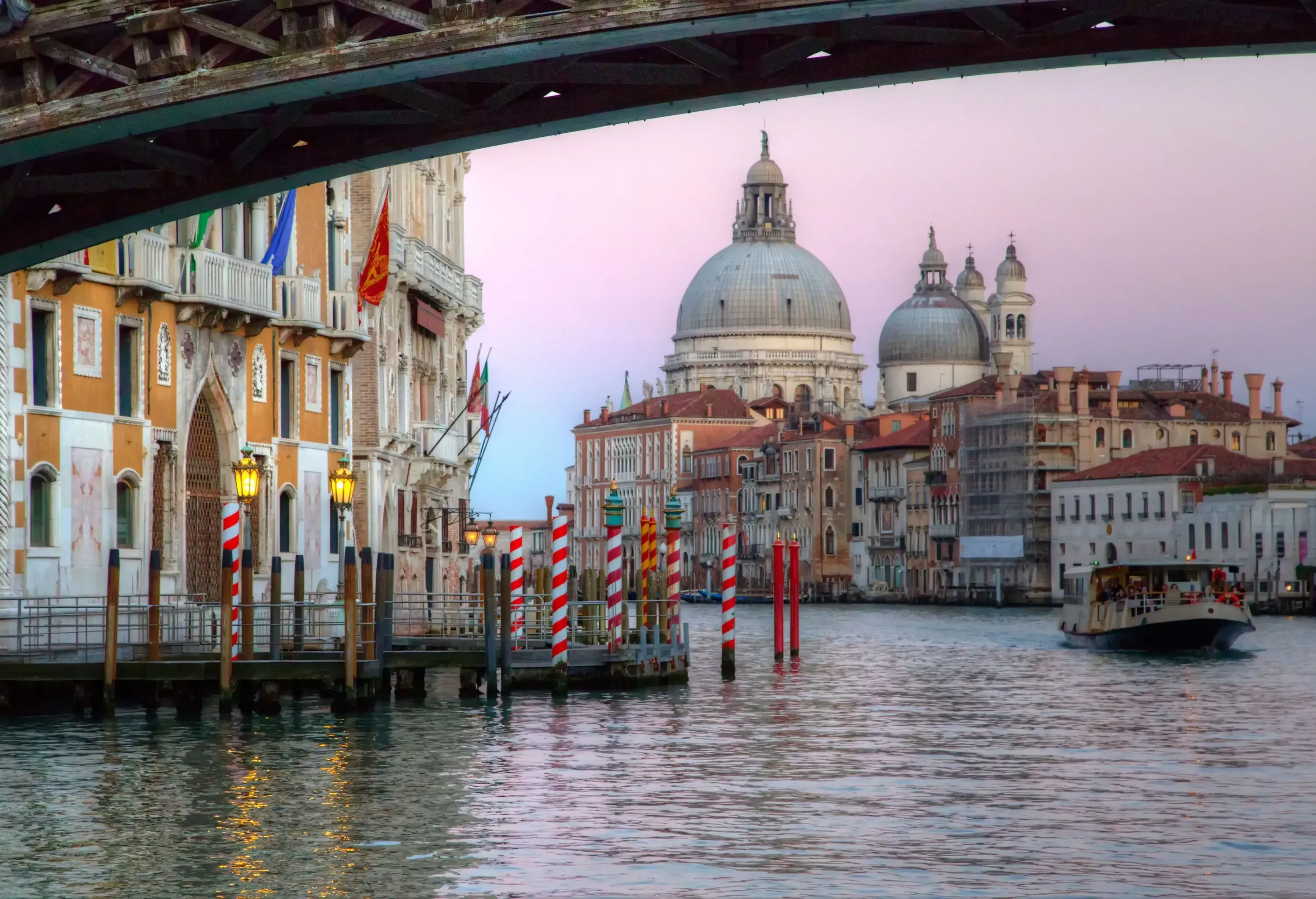 A boat cruises across a water canal near a harbour against a backdrop of domed structures with cupolas.
