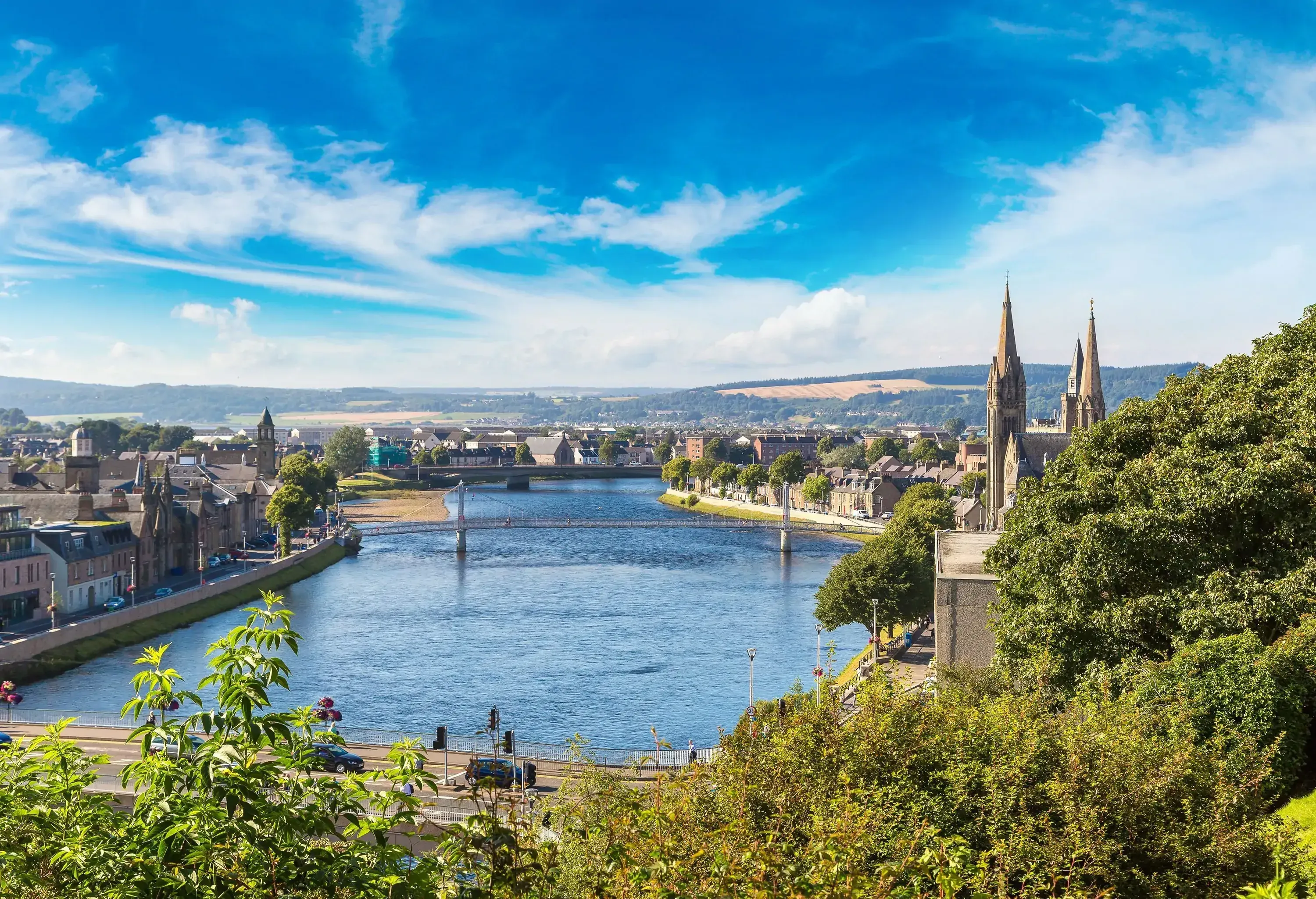 A picturesque cityscape by the river with classic houses ad buildings against the cloudy blue sky.
