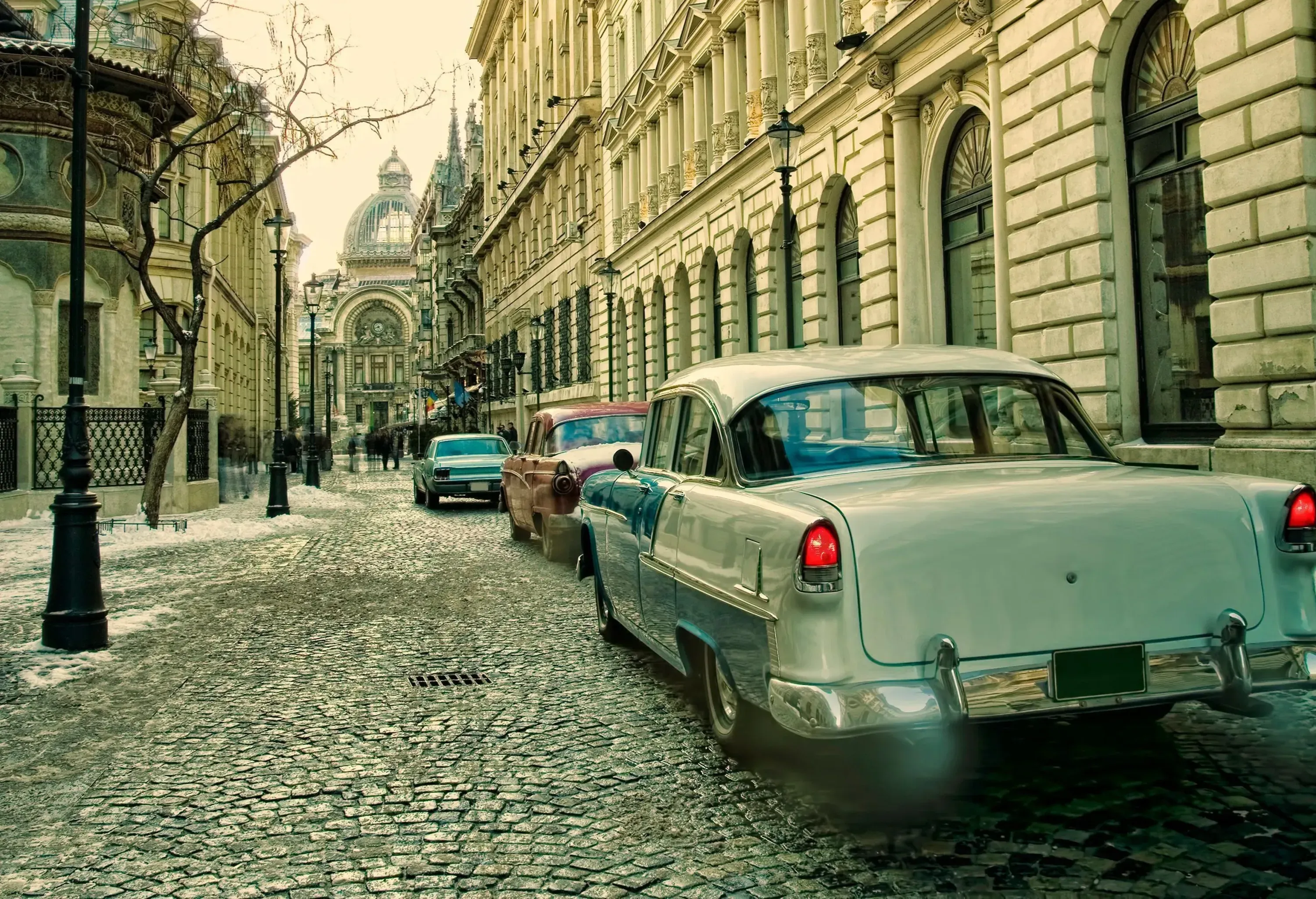 Vintage cars parked on one side of a cobbled street lined with lampposts amidst the medieval buildings.
